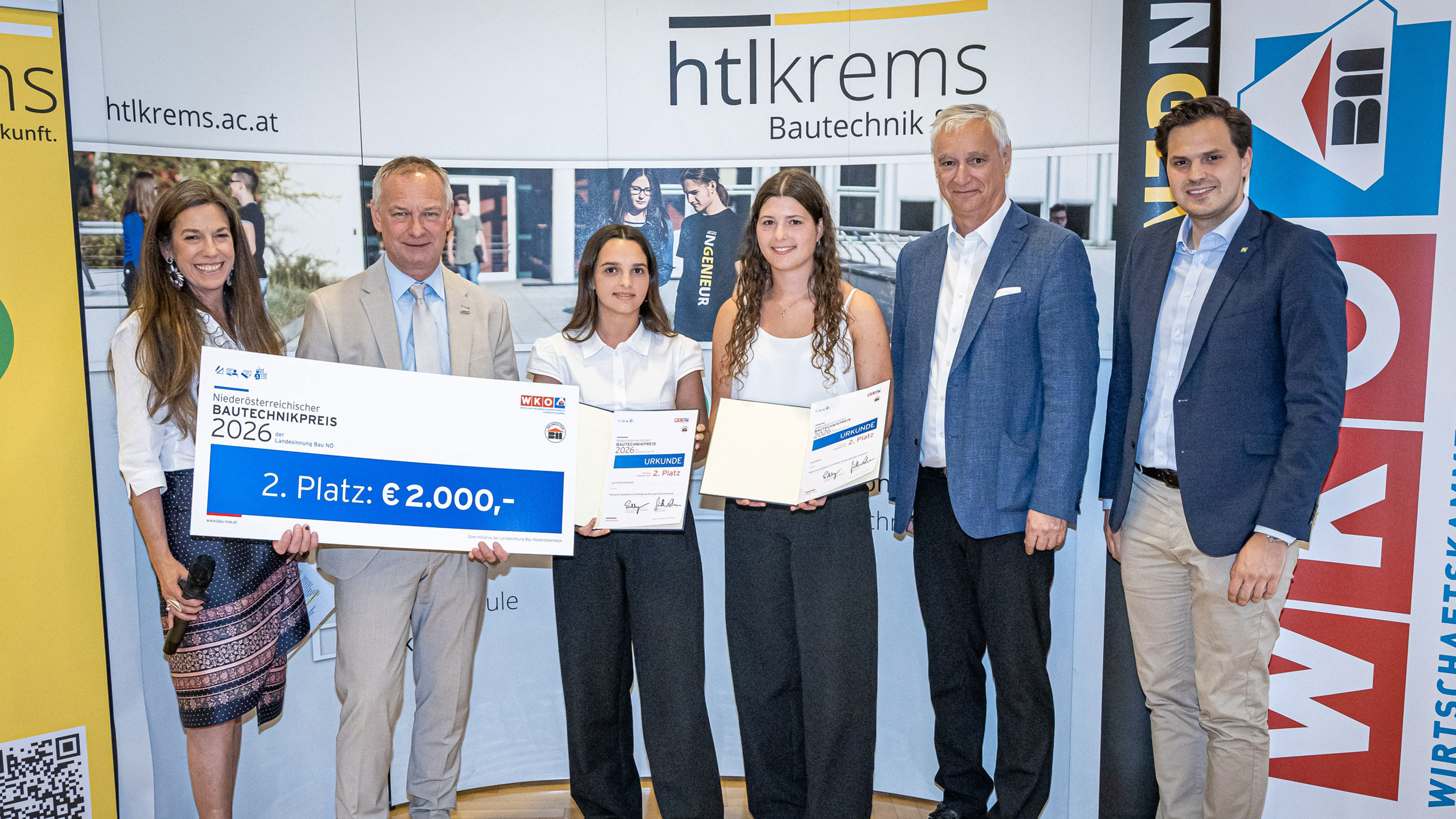 Gruppe von Personen bei einer Preisverleihung vor einer HTL‑Krems‑Fotowand, eine Person h&auml;lt einen Scheck mit der Aufschrift Bautechnikpreis 2026 &ndash; 2. Platz: 2.000 Euro.