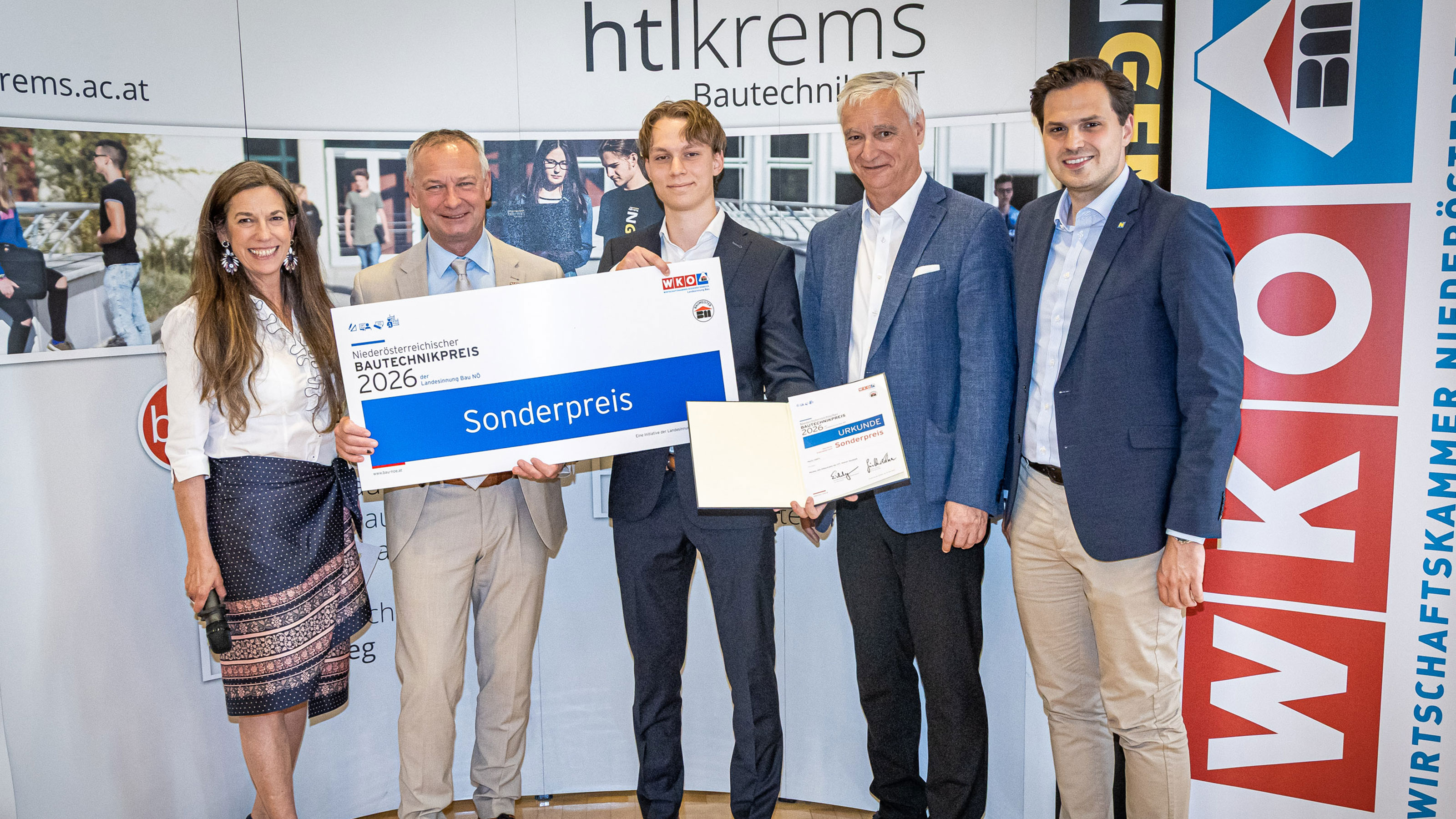 Gruppe von Personen bei einer Preisverleihung vor einer HTL‑Krems‑Fotowand, eine Person h&auml;lt einen Scheck mit der Aufschrift Bautechnikpreis 2026 &ndash; Sonderpreis.