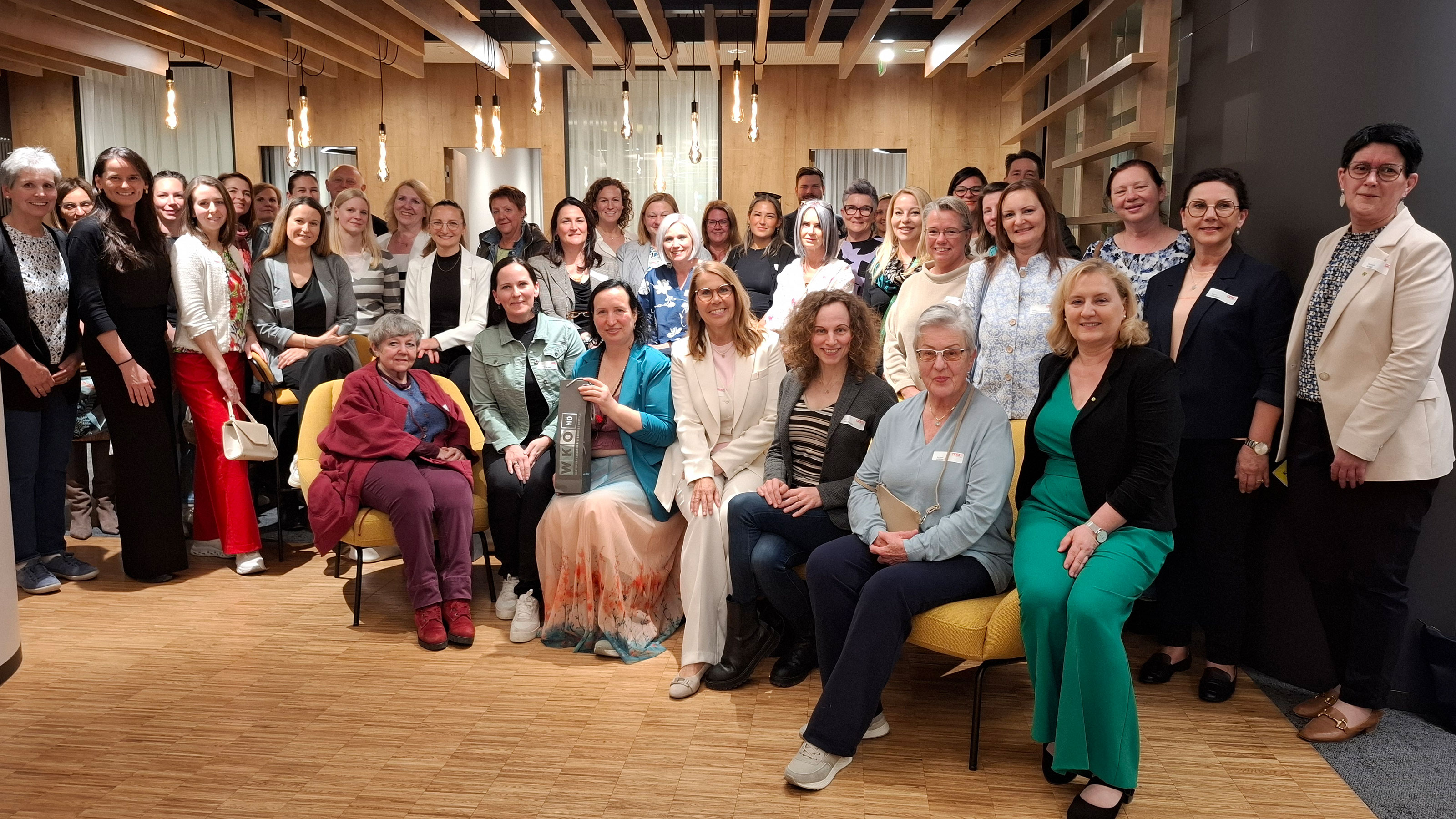 Gruppenfoto von rund 30 Teilnehmenden bei einem After-Work-Treffen in einem modern gestalteten Innenraum mit Holzdecke, Sitzgelegenheiten und Stehbereich.