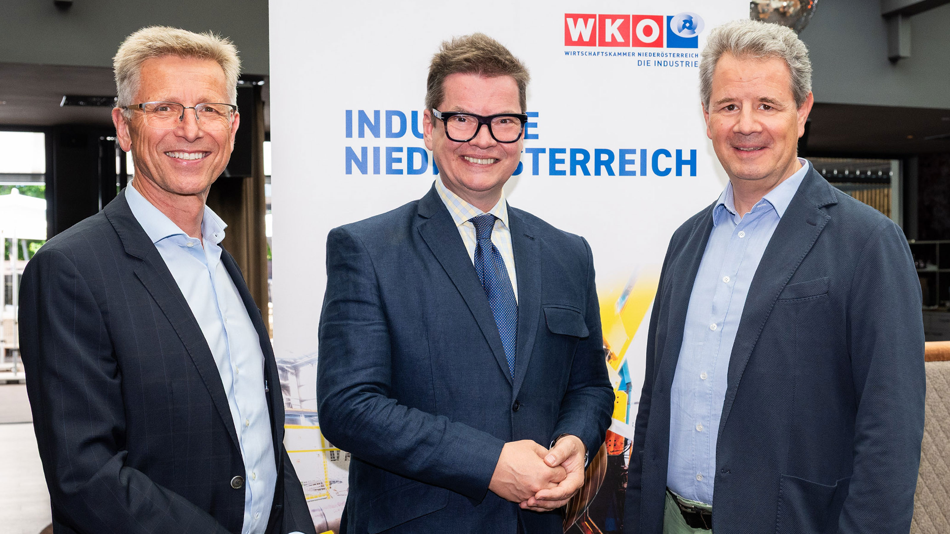 Drei Personen stehen bei einer Veranstaltung vor einem Banner mit der Aufschrift "Industrie Nieder&ouml;sterreich&lsquo;" und WKN&Ouml;‑Logo.