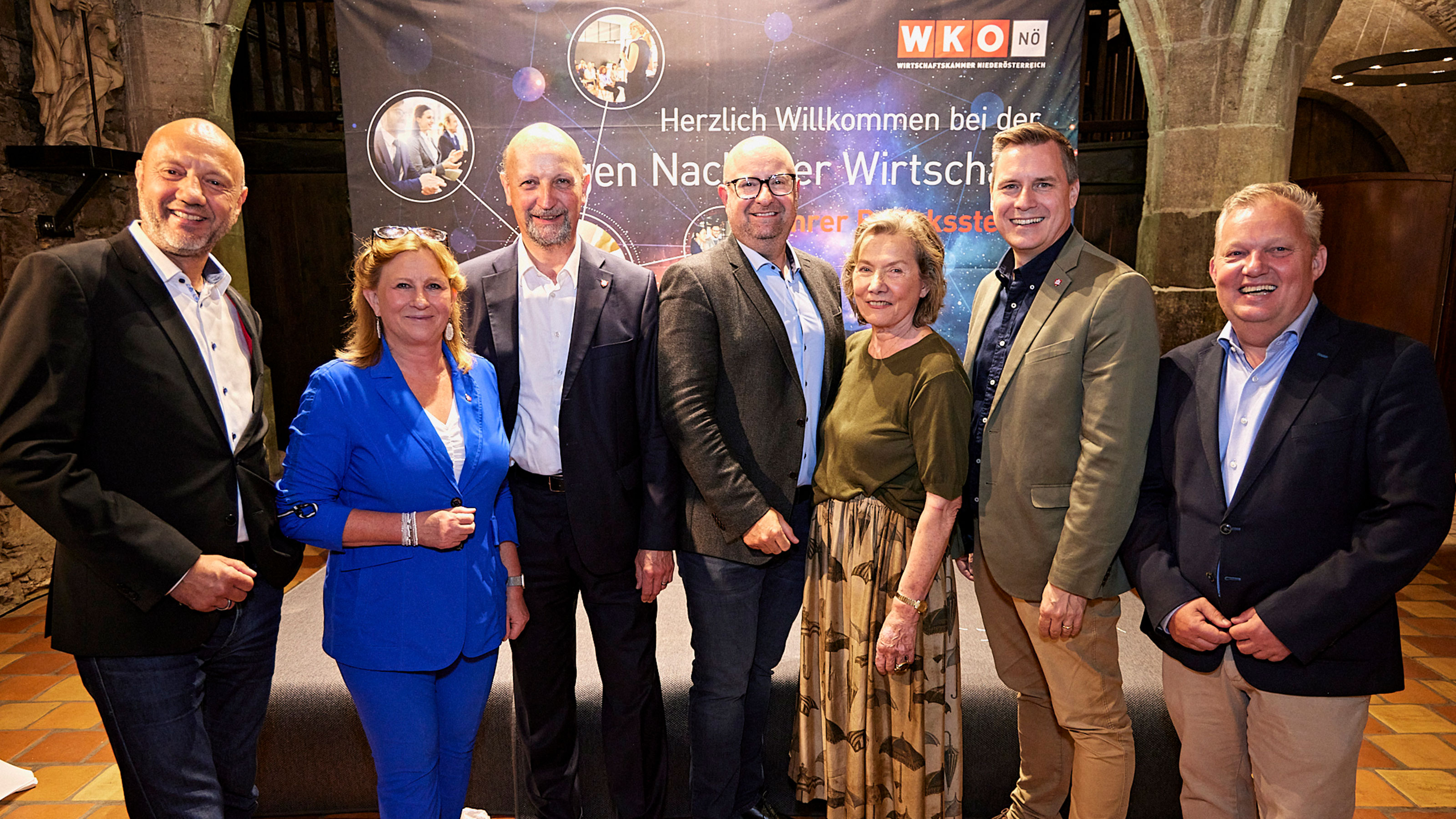 Gruppenfoto vor WKO‑N&Ouml;‑Banner: Mehrere Personen stehen nebeneinander in einem historischen Innenraum und posieren f&uuml;r ein Erinnerungsfoto bei einer Wirtschaftskammer‑Veranstaltung.