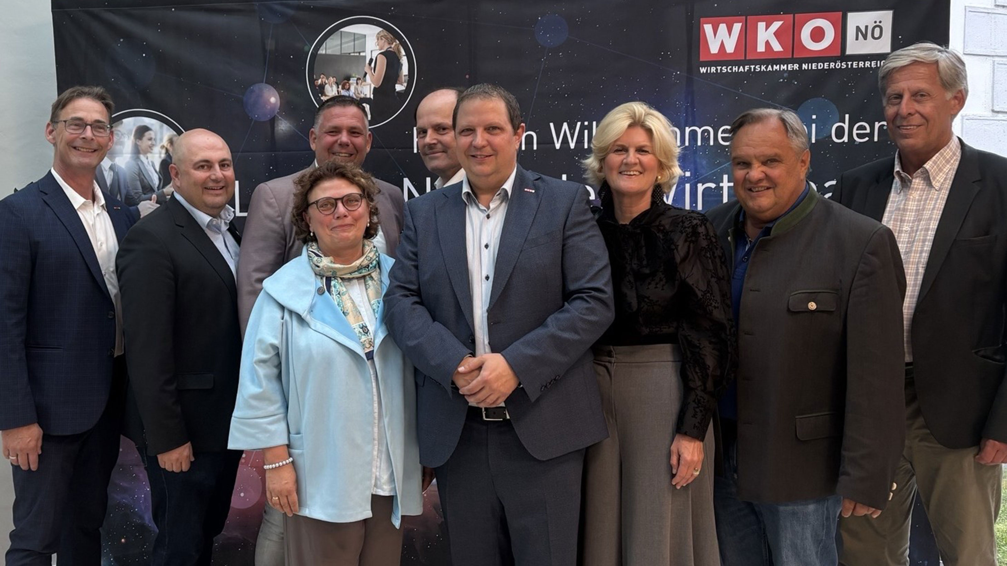 Gruppenfoto von neun Personen vor einem WKO‑N&Ouml;‑Banner in einem Innenraum, nebeneinander stehend und zur Kamera ausgerichtet.