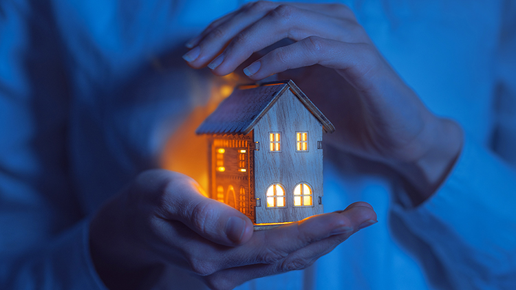 Handpaar leuchtendes Miniaturhaus haltend