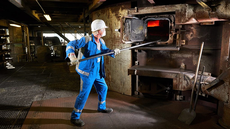 Arbeiter mit Helm schaufelt in einen Ofen