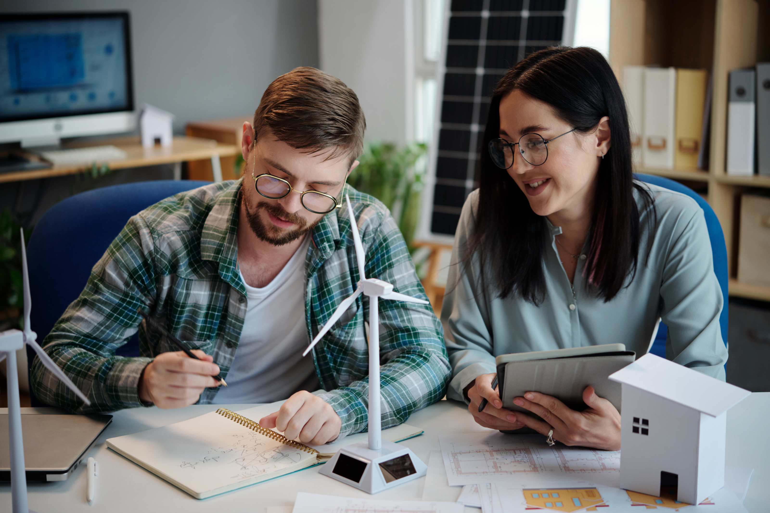 Zwei Personen mit Brillen &uuml;ber Schreibtisch mit Modellen von Windr&auml;dern gebeugt