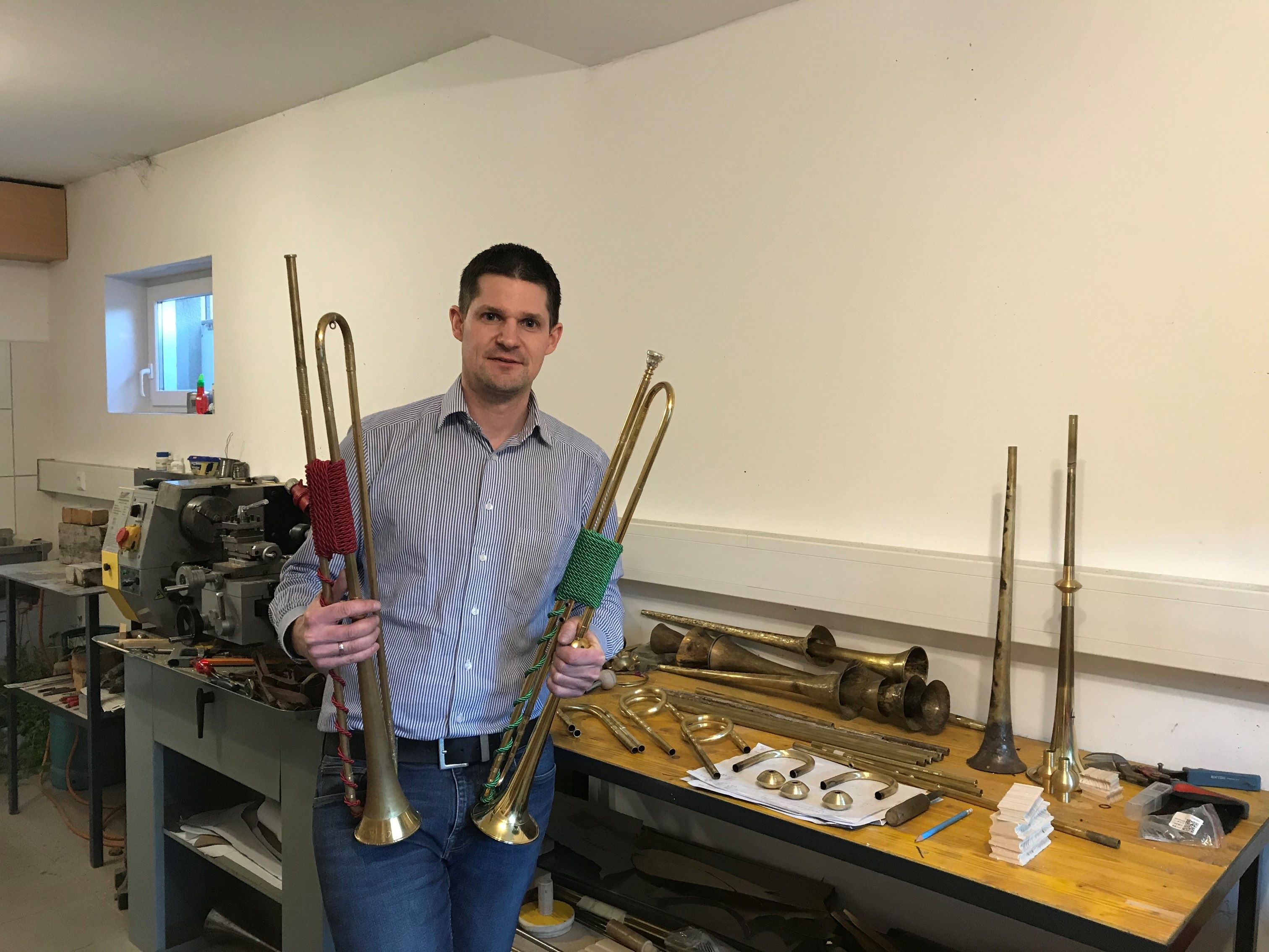 Harald Schuh steht mit zwei Barocktrompeten in den Händen in einer Werkstatt