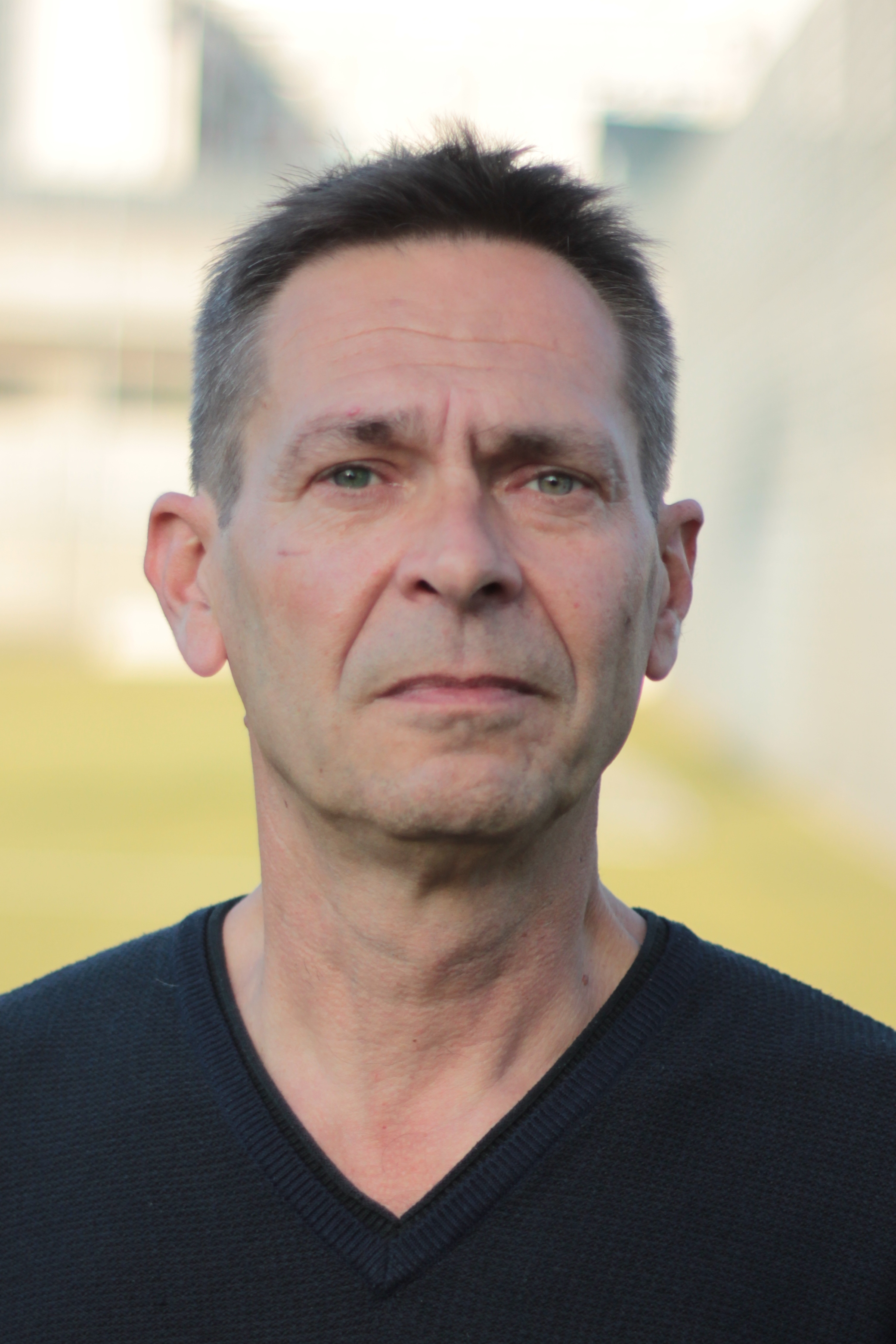 Portr&auml;tfoto: Person mit kurzen dunklen Haaren und gr&uuml;nlichen Augen vor unscharfem Hintergrund