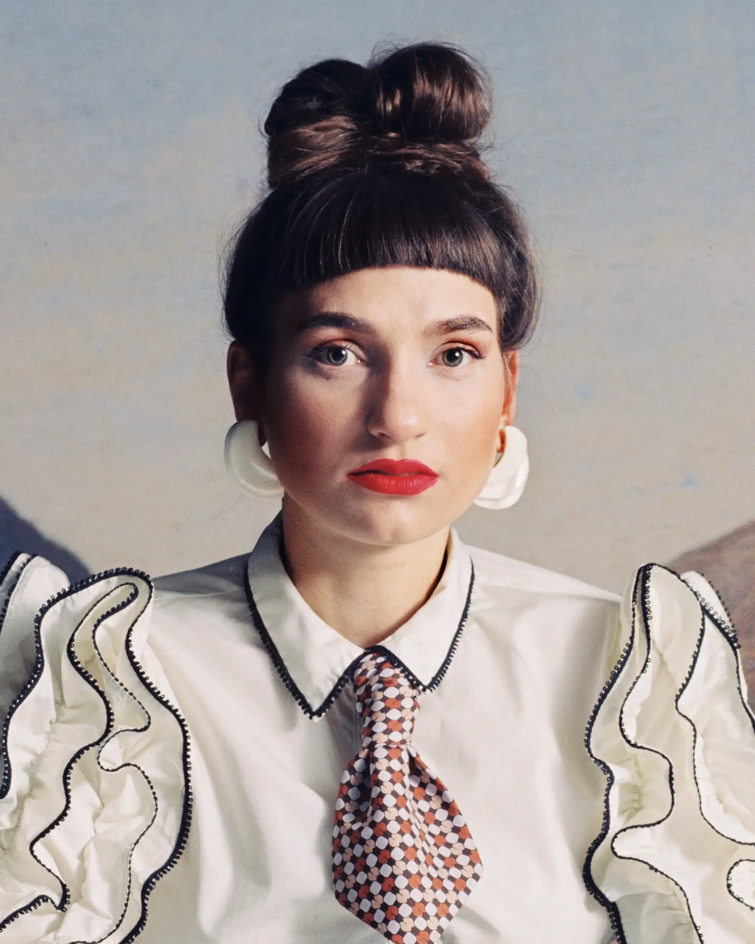 Portr&auml;t einer Person mit hochgestecktem Haar, wei&szlig;er R&uuml;schenbluse, Krawatte und gro&szlig;en Ohrringen