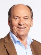 Portr&auml;t einer Person mit braunem Sakko und hellblauem Hemd vor hellem Hintergrund.