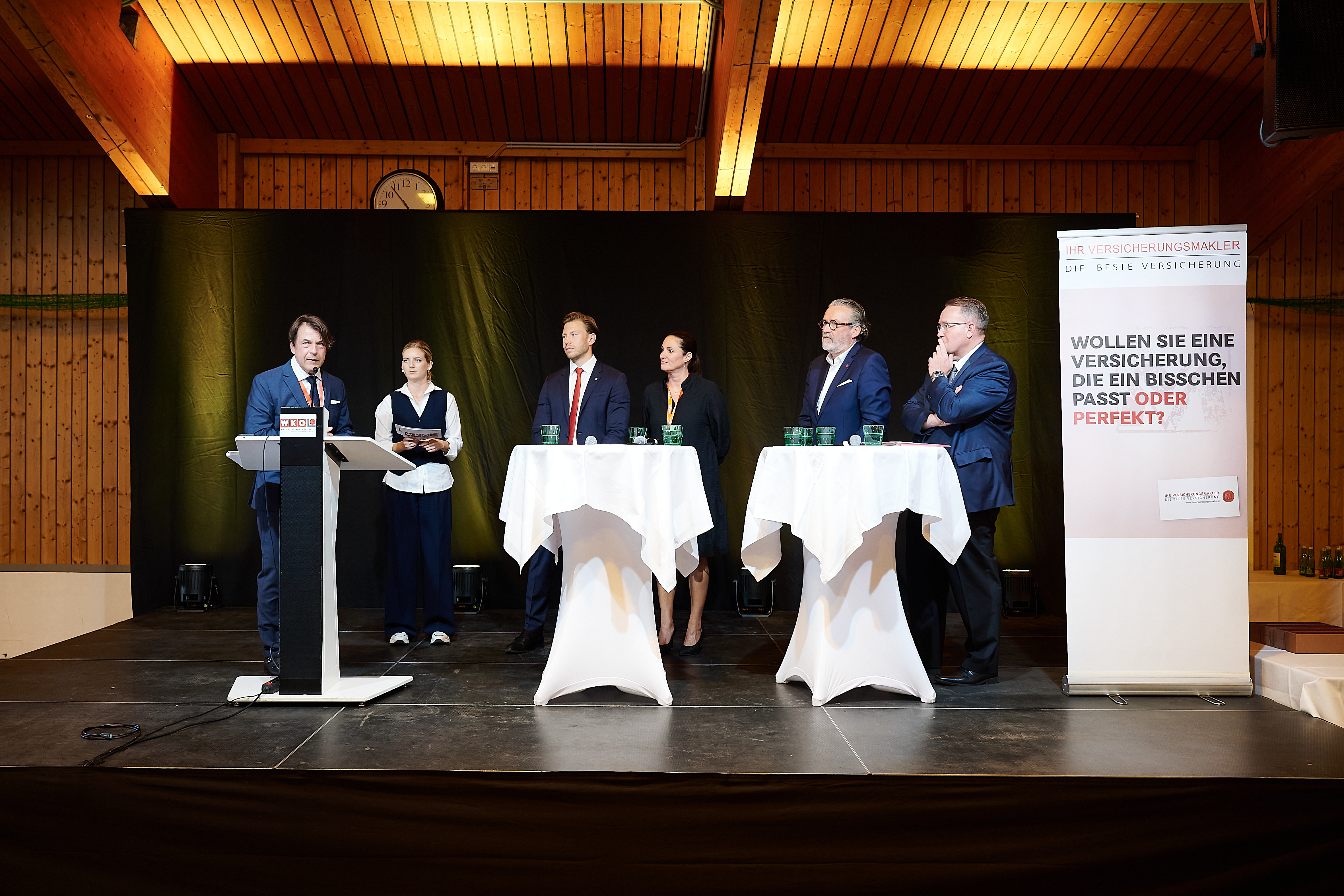 Sechs Personen bei einer Veranstaltung auf einer B&uuml;hne, eine Person spricht am WKO Rednerpult.