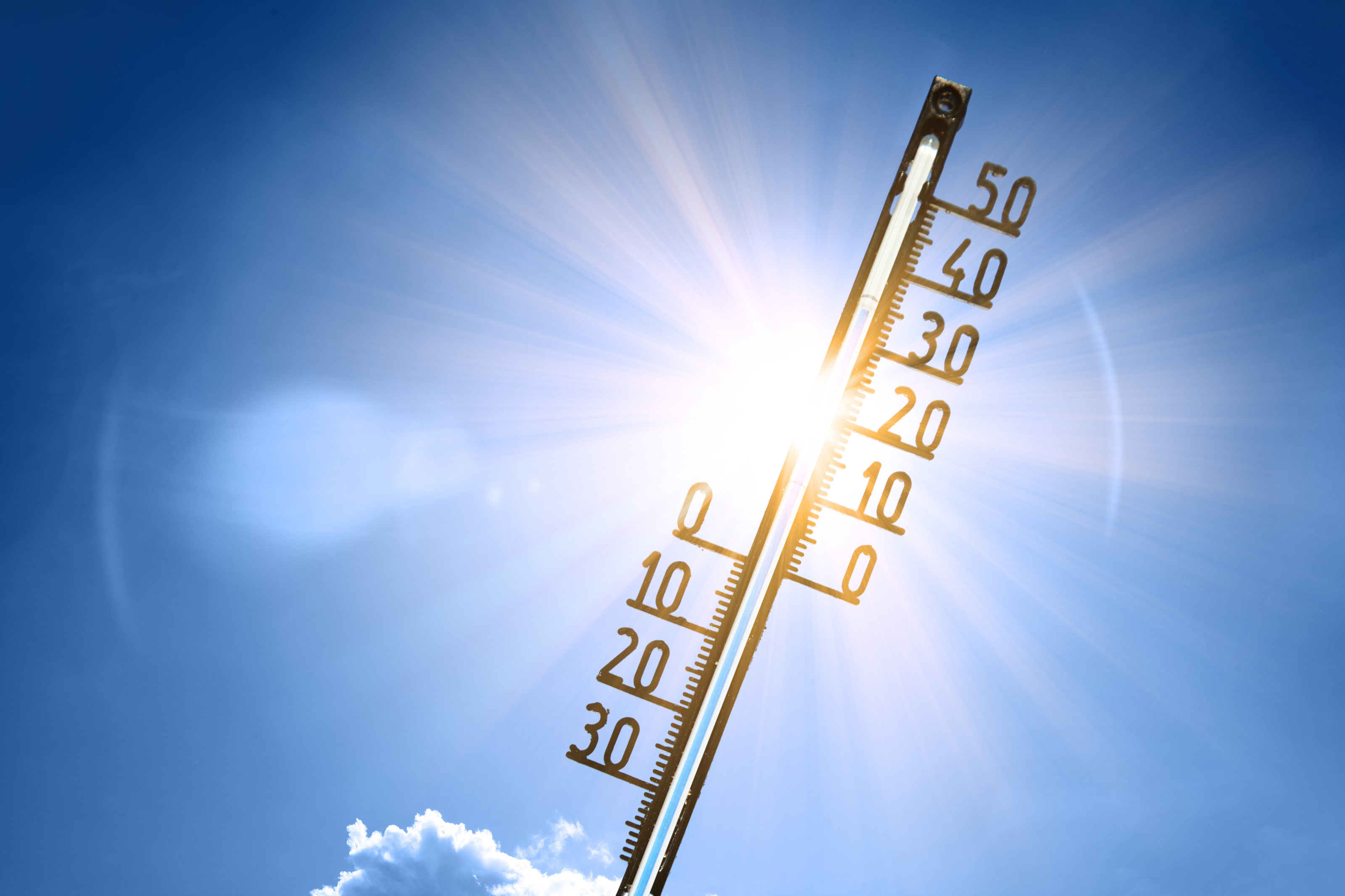 Nahaufnahme eines Thermometers vor dem Hintergrund eines blauen Himmels mit ein paar Wolken. Rechts sind die Zahlen bis 50 daran montiert. Das Thermometer wird von strahlendem Sonnenlicht beleuchtet