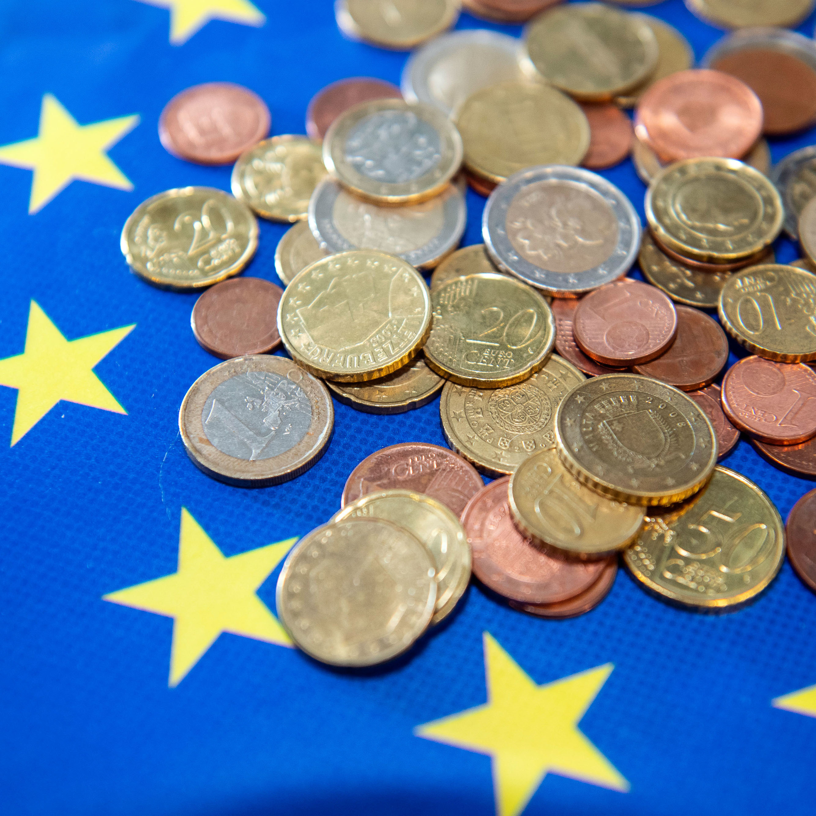 Detailansicht unterschiedlicher Euromünzen auf blauem Untergrund mit gelben Sternen