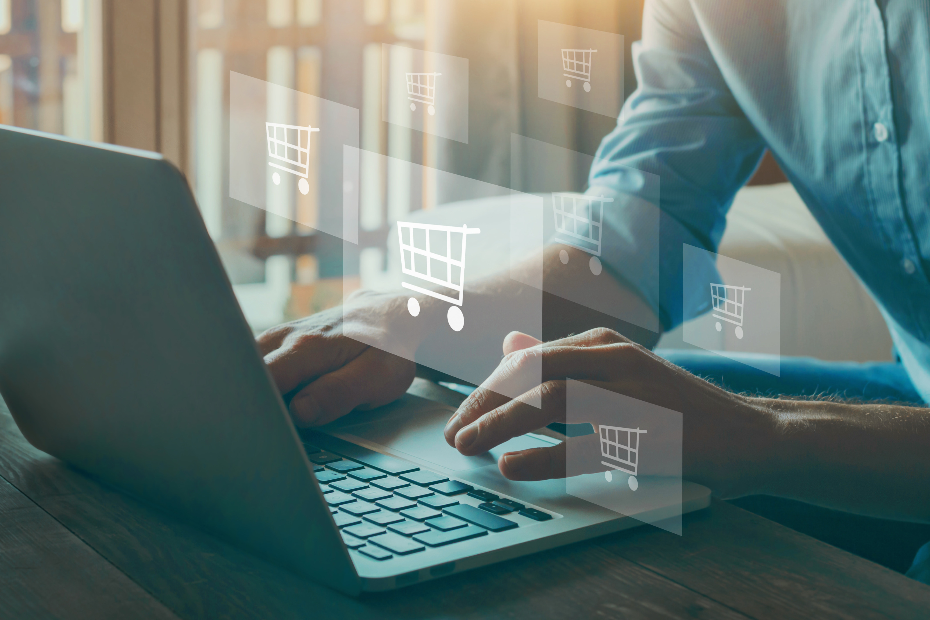 Detailansicht tippender H&auml;nde auf Notebook-Tastatur, dar&uuml;ber Symbole eines Einkaufswagens