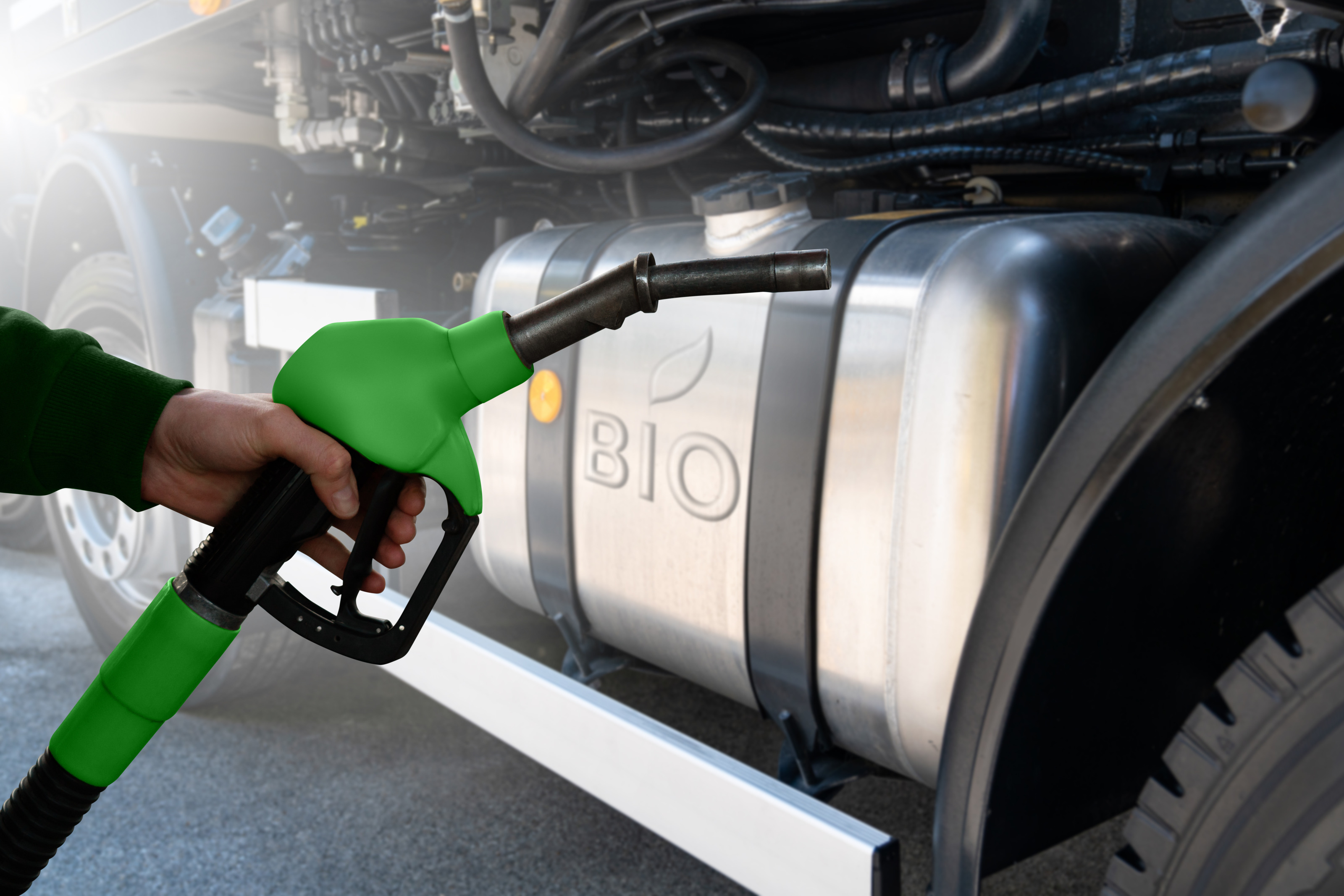 Detailansicht eines grünschwarzen Treibstoffzapfhahnes von Hand gehalten, im Hintergrund Tank eine Gefährtes mit der Aufschrift Bio