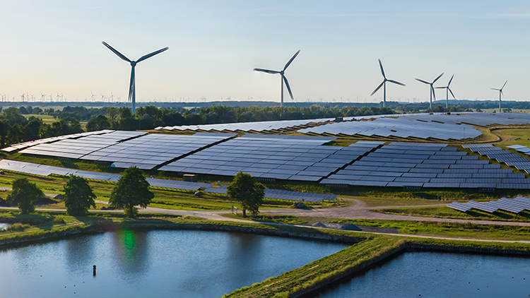Feld mit Solarpanelen und Windkrafträdern umgeben von grüner Landschaft und Wasser