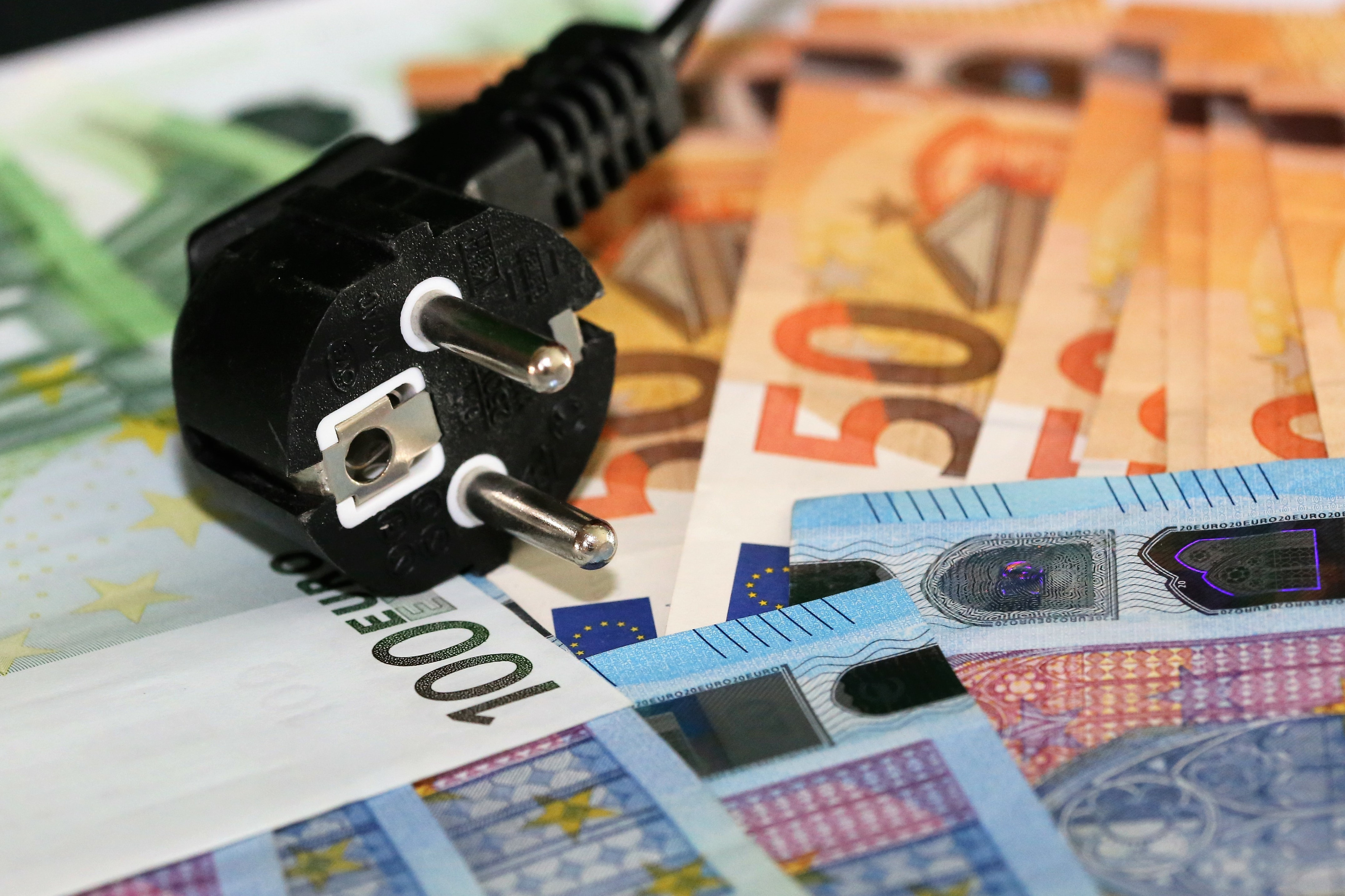 Nahaufnahme mehrerer Euroscheine, wie zwanzig, f&uuml;nfzig oder hundert Euro. Auf den Scheinen liegt das Ende eines Kabels mit Stecker.