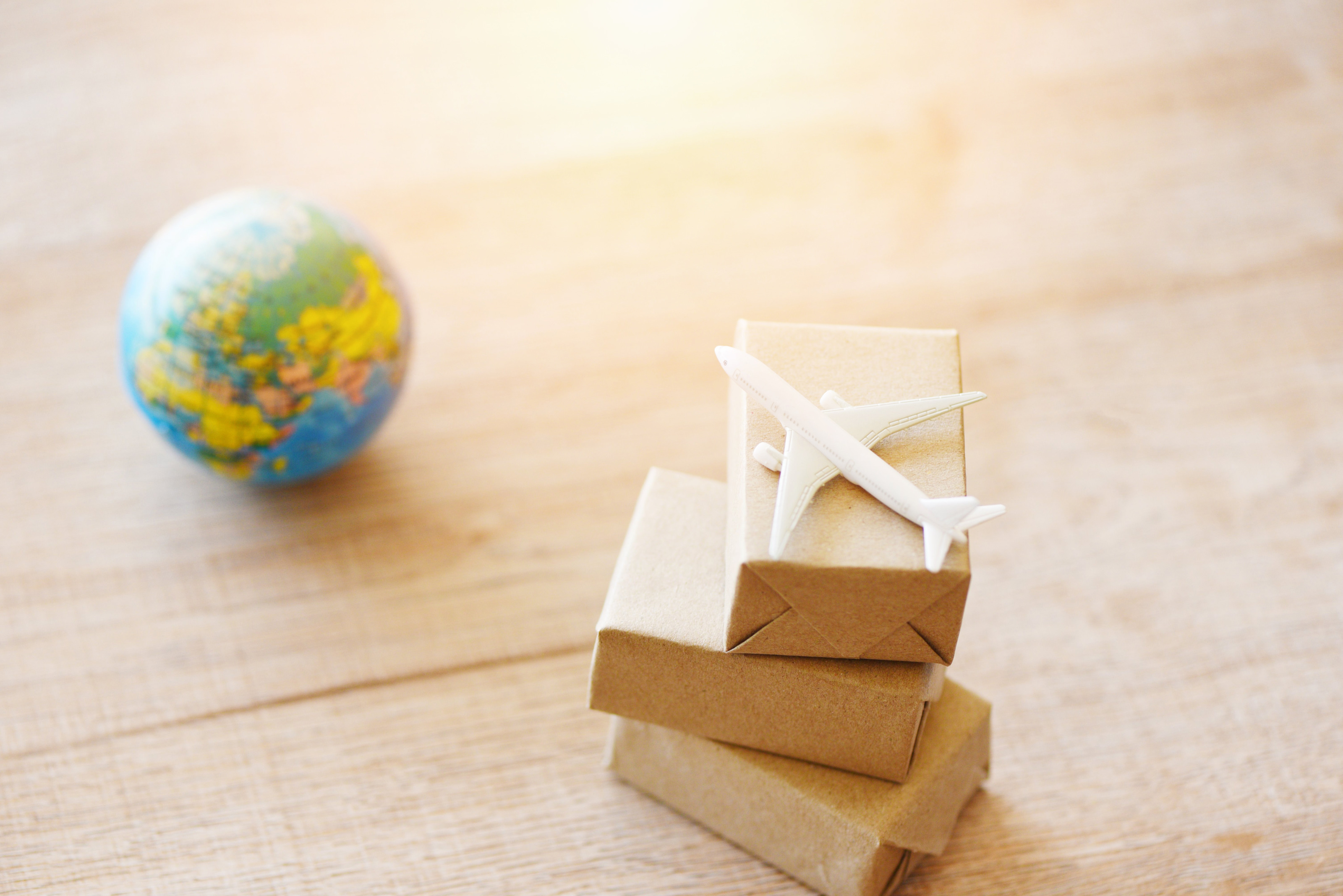 Miniaturpakete mit einem Miniaturflugzeug sind auf einem Holzuntergrund platziert, daneben ist ebenso ein Miniaturglobus