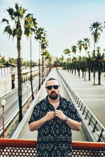 Person mit Sonnenbrille steht auf Weg mit Palmenreihen und Gel&auml;nder