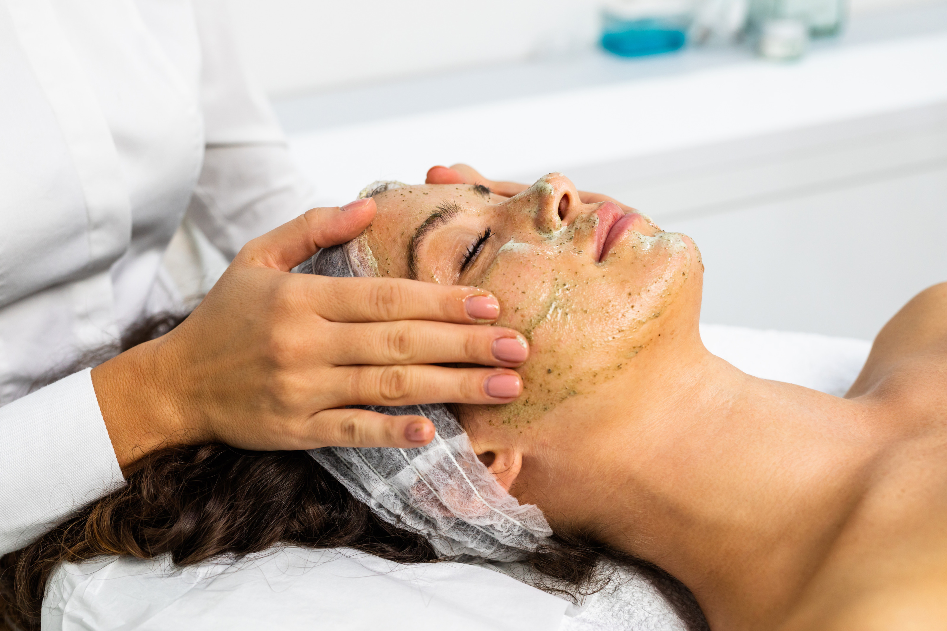 Nahaufnahme einer Gesichtsbehandlung, bei der die Kosmetikerin das Gesicht der Kundin mit einem Peeling massiert.