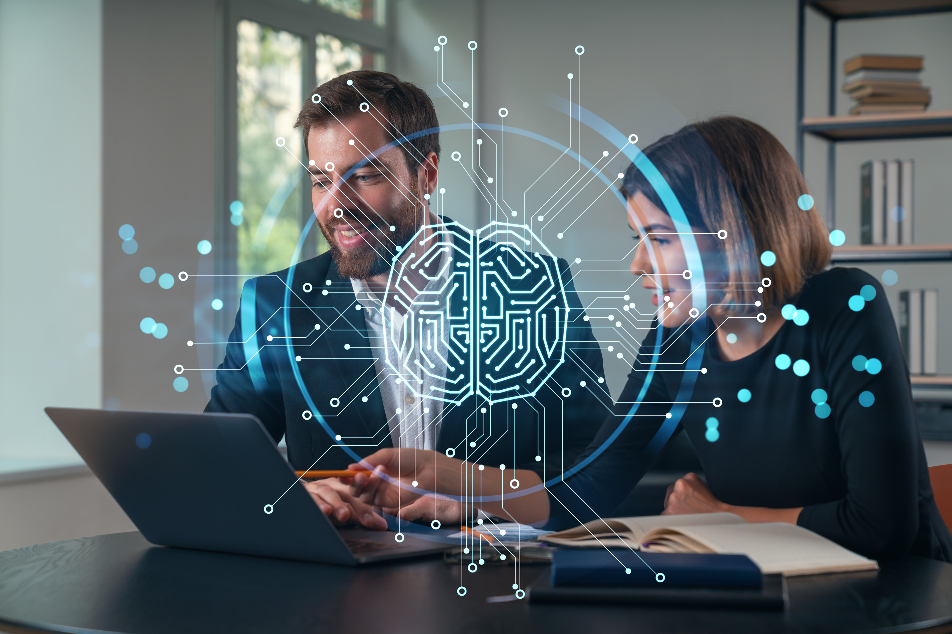 Zwei Personen sitzen hinter einem Tisch. Vor ihnen ist ein aufgeklappter Laptop. Beide blicken darauf. &Uuml;ber dem Bild ist eine Grafik eines Kreises, in dem verschiedene Linien und Punkte sind, die ein Gehirn darstellen.