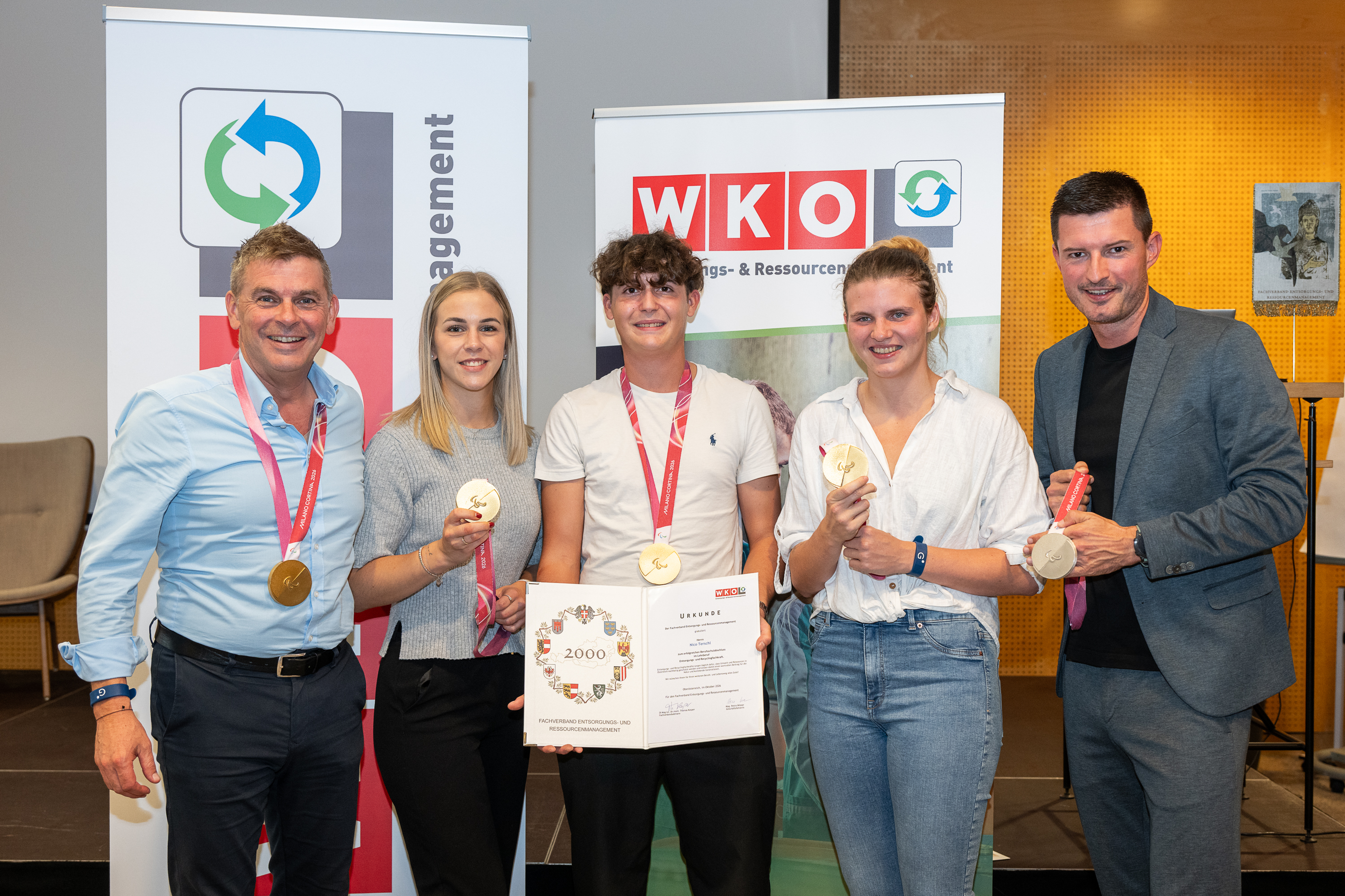 Fünf Personen stehen vor WKO Roll-ups. Vier präsentieren Medaillen, eine Person hält eine Urkunde.