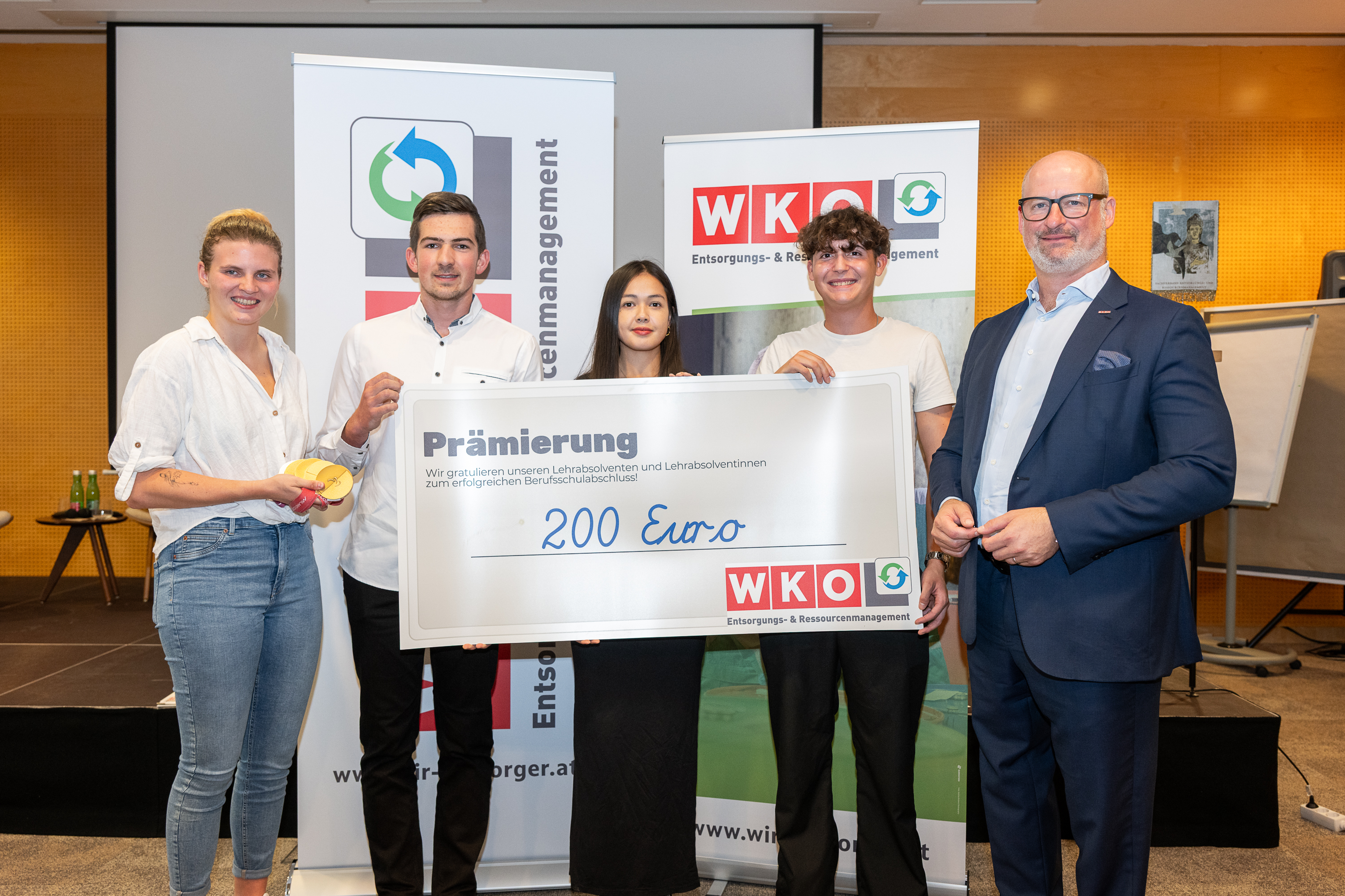 Fünf Personen stehen mit einem symbolischen WKO Scheck über 200 Euro für die Prämierung von Lehrabschlüssen.
