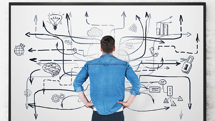 Person in R&uuml;ckenansicht steht vor Tafel mit verschlungenen Linien