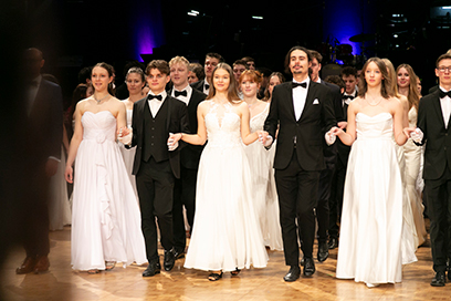 Personen auf Tanzfläche in weißer und schwarzer Abendgarderobe in Polonaiseaufstellung