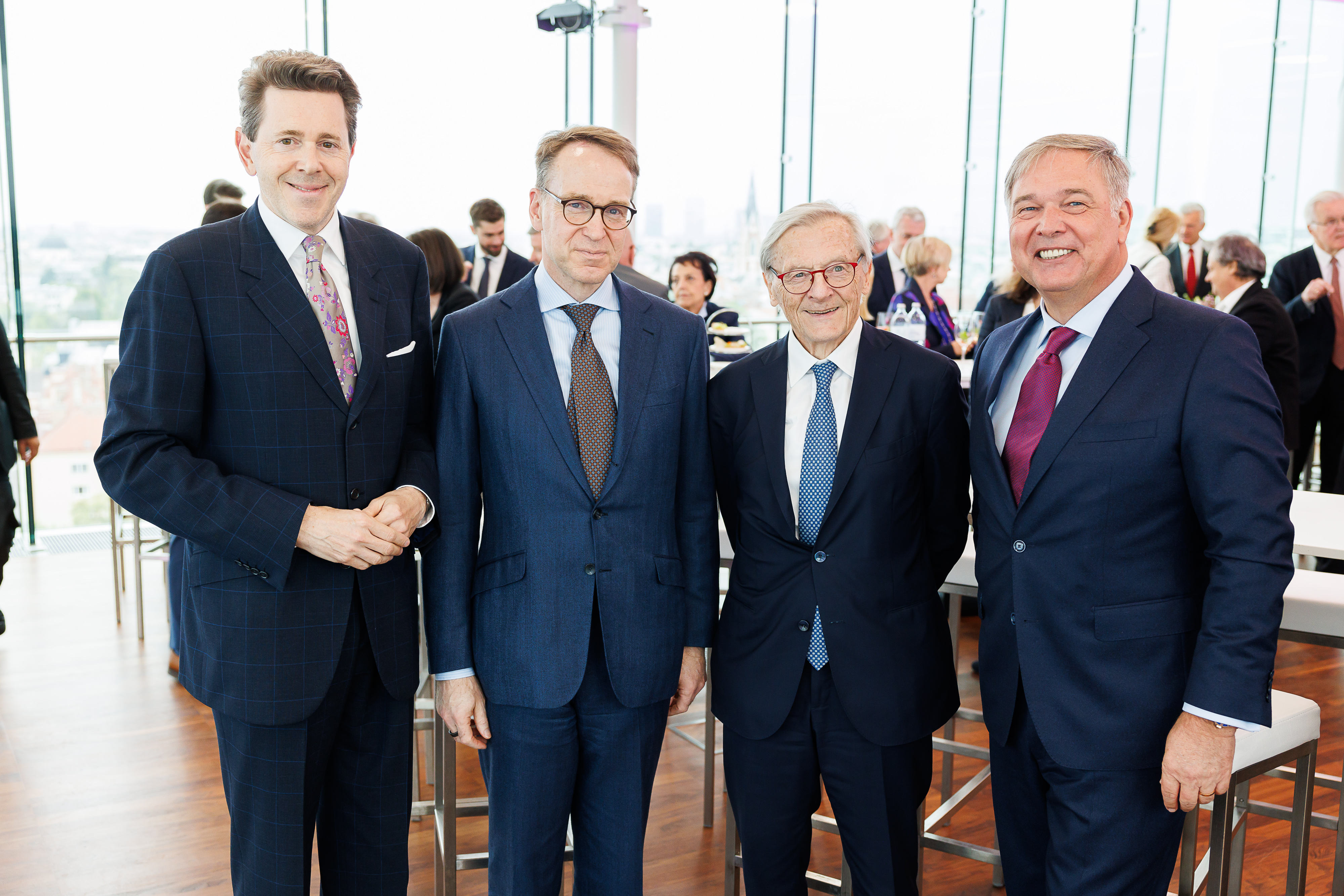 Vier schick gekleidete Personen stehen nebeneinander und lächeln in die Kamera