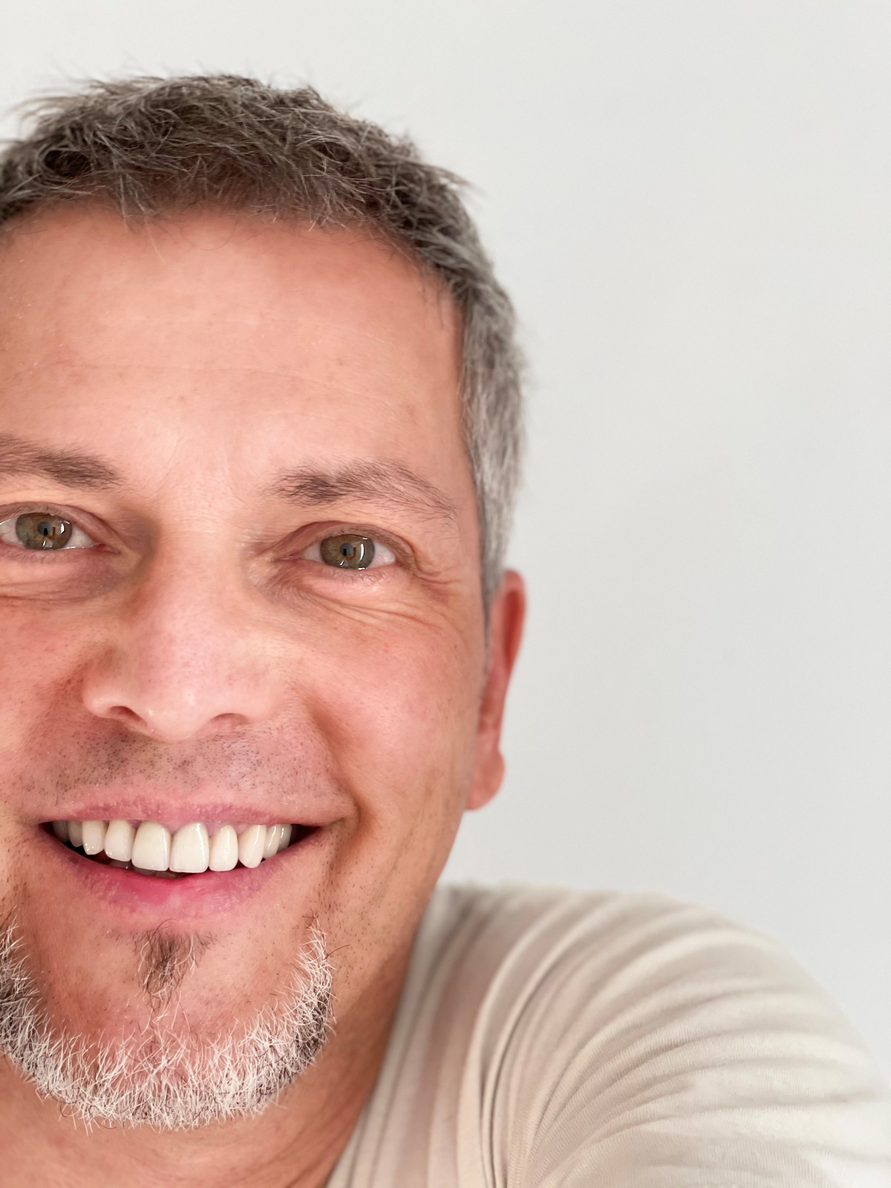 Portr&auml;tfoto einer l&auml;chelnden Person mit grauem Haar vor hellem Hintergrund