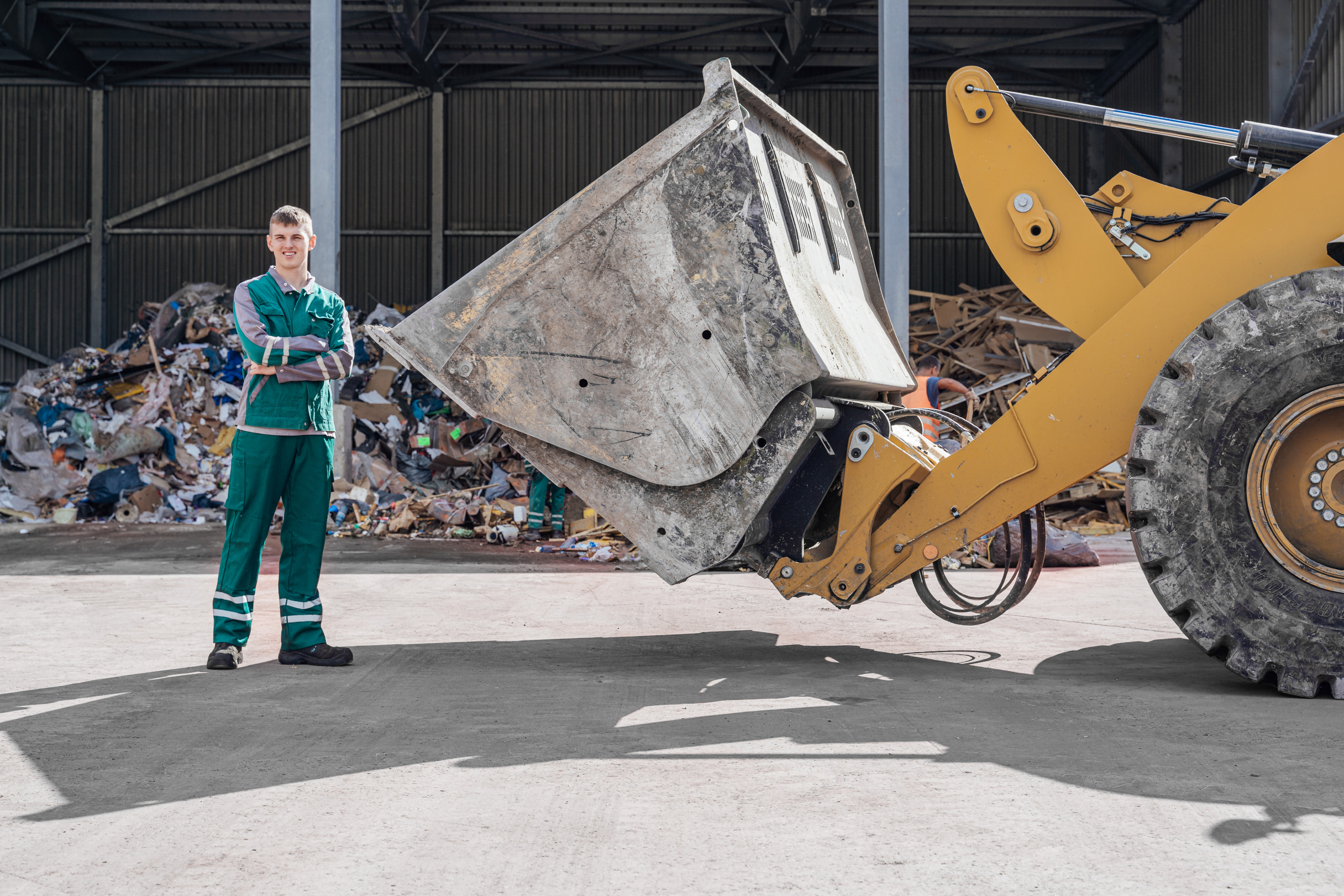 Lehrling der Abfallwirtschaft neben einer Baggerschaufel