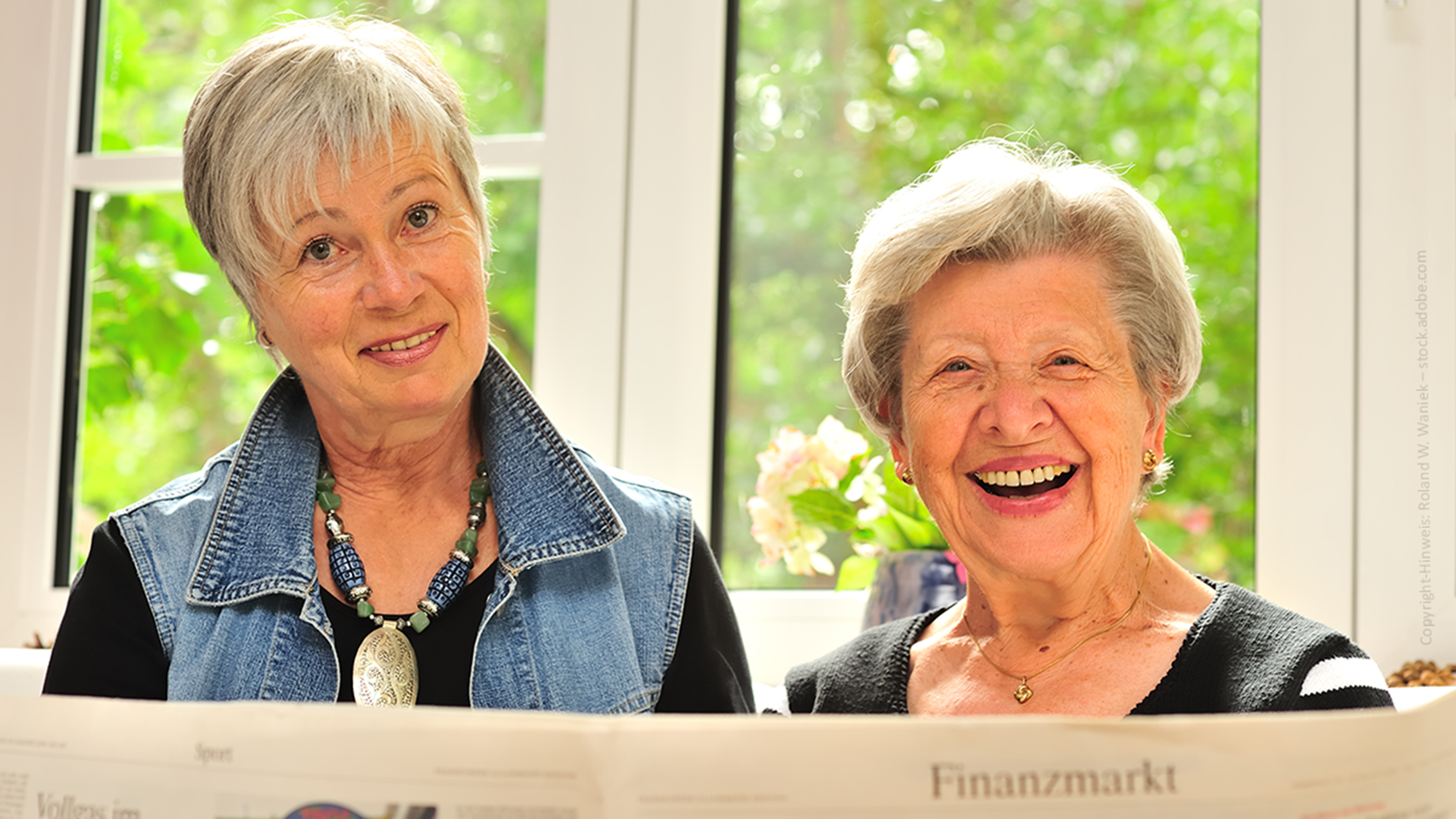 zwei ältere Frauen mit kurzen grauen Haaren, die in die Kamera sehen und eine Zeitschrift in der Hand halten