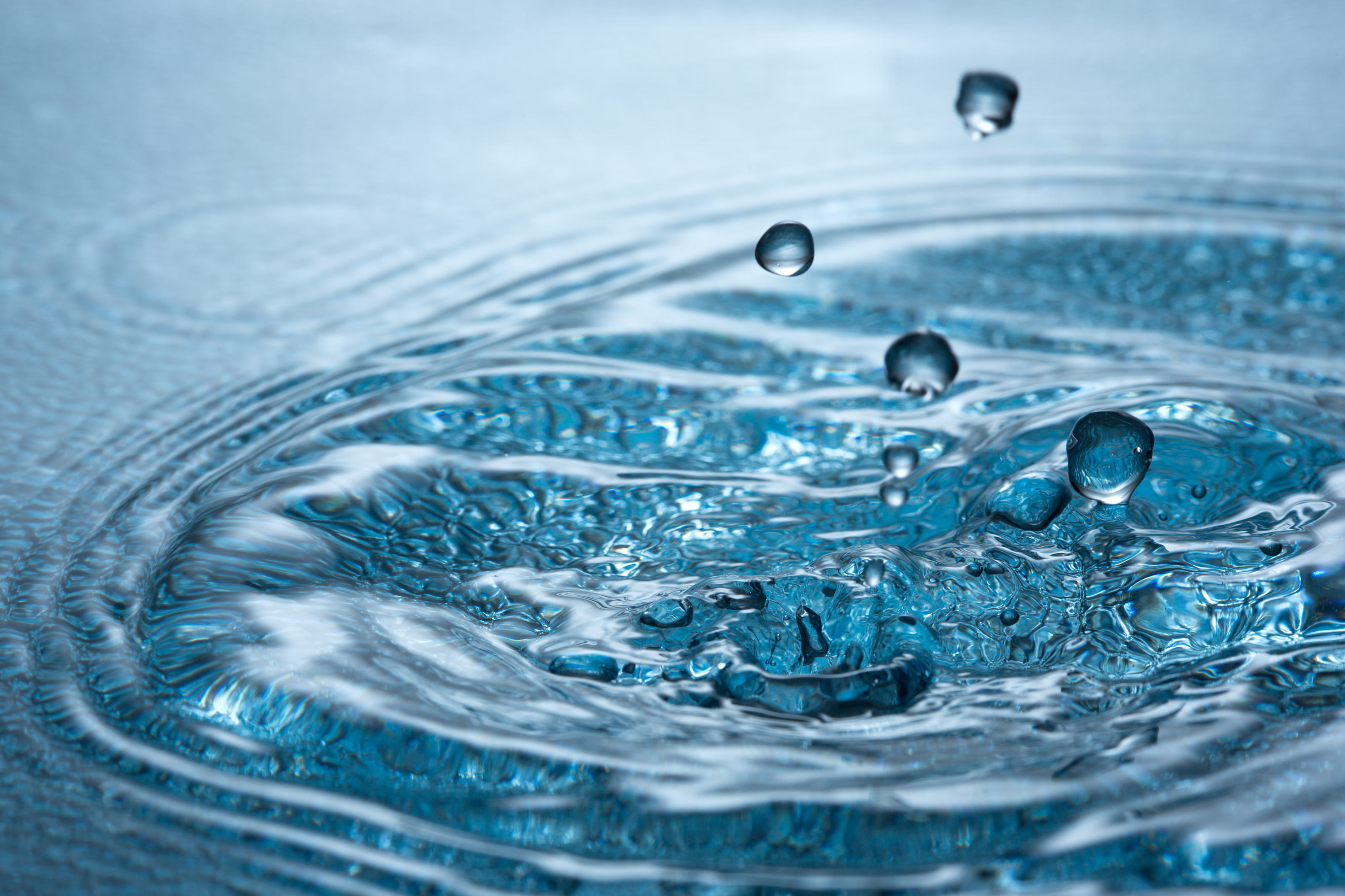 Nahaufnahme eines Wassers, in das ein paar Wassertropfen fallen und Wellen schl&auml;gt.