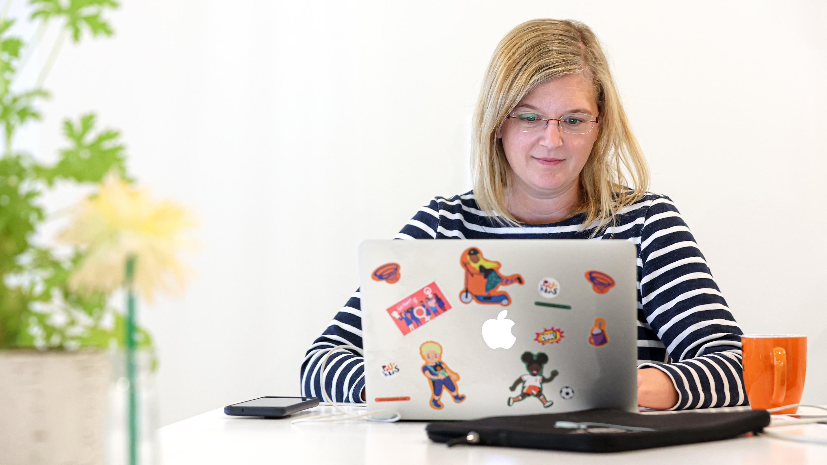 Cornelia Aigenberger sitzt vor ihrem Macbook an einem Schreibtisch