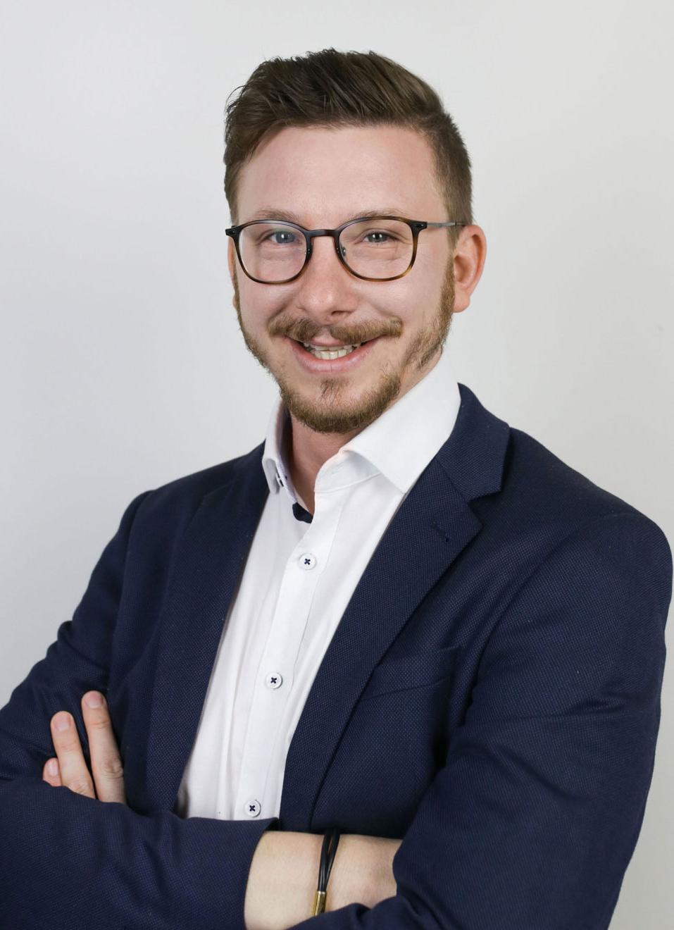 Vortragender Herr Florian Radeschnig, Mann mit kurzen dunklen Haaren, Brille und Bart, tr&auml;gt ein wei&szlig;es Hemd und ein schwarzes Sakko