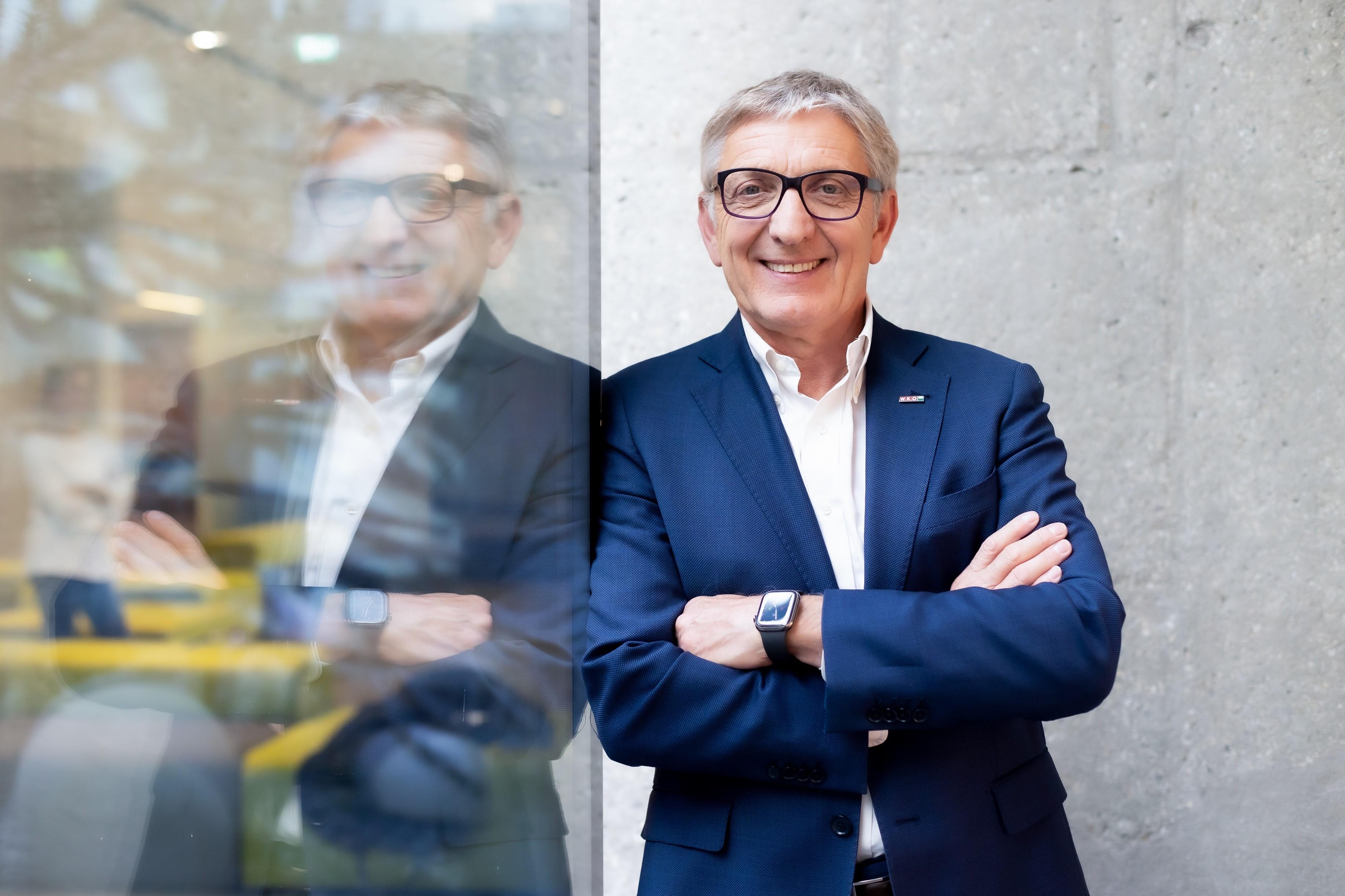 Portr&auml;t von WKO Steiermark Pr&auml;sident Josef Herk, der an eine Glasscheibe lehn in welcher er sich spiegelt