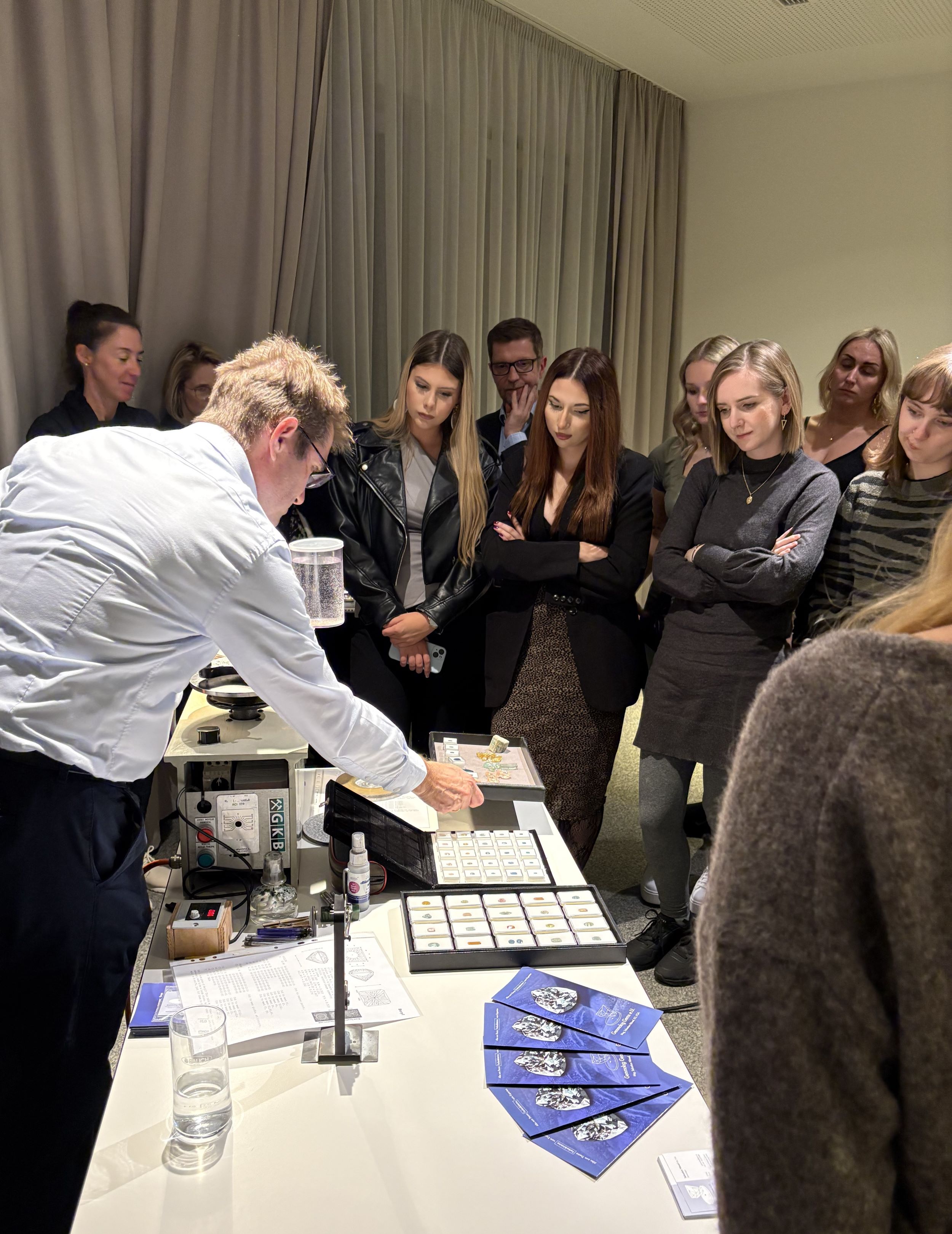 Vortragender präsentiert verschiedene Edelsteine an einem Tisch einer Gruppe von Teilnehmer:innen der Veranstaltung