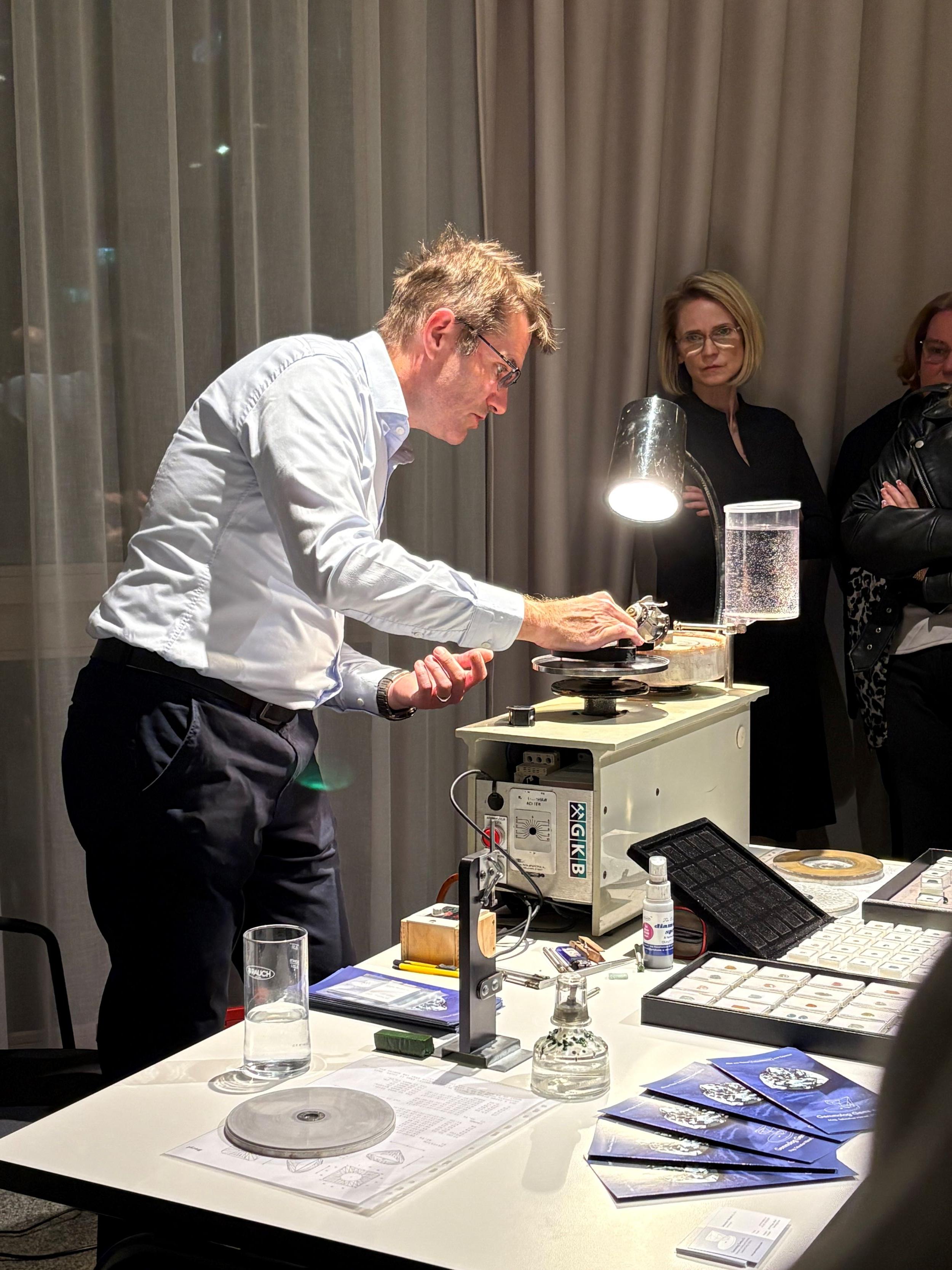 ein Gemmologe führt gerade das Schleifen eines Edelsteines aus und das Publikum sieht zu