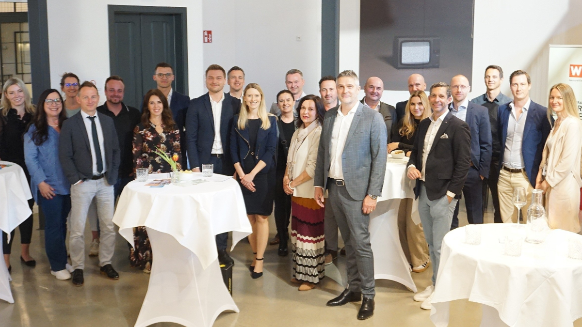 Gruppenfoto von Frauen und M&auml;nnern im Businessoutfit, die zwischen Stehtischen stehen