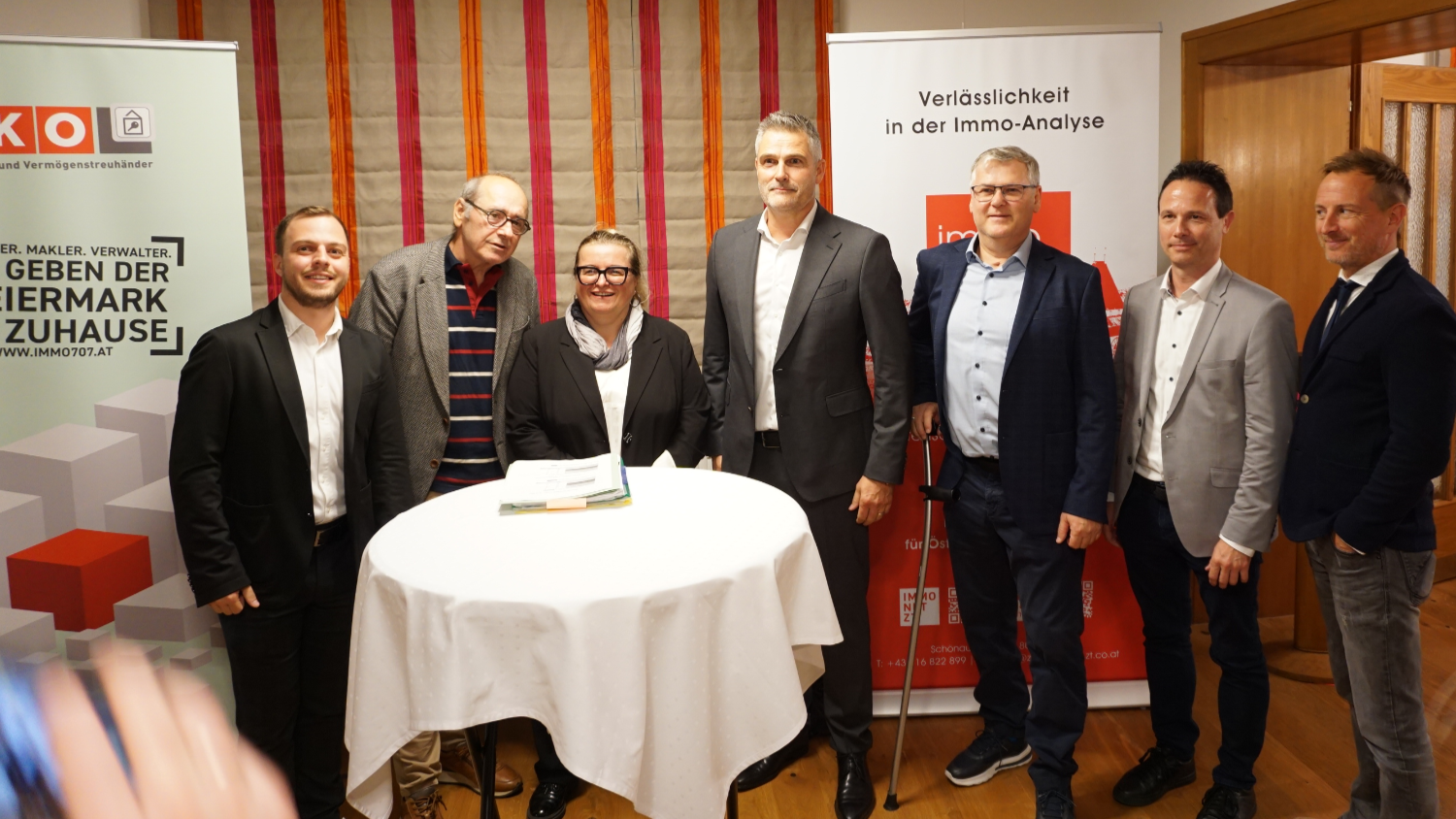Gruppenfoto von sechs M&auml;nnern und einer Frau in Businesskleidung bei einer Immobilienveranstaltung, vor Werbebannern der WKO Steiermark und der Immobilienanalyse