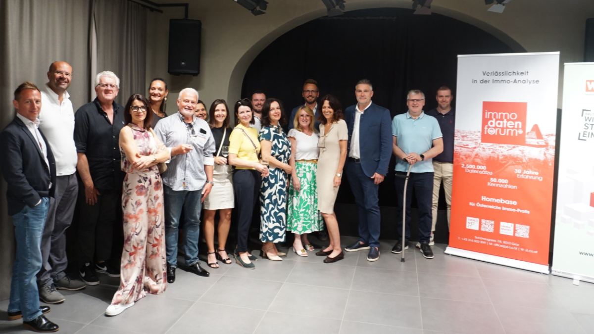 Gruppenfoto von M&auml;nnern und Frauen im sommerlichen Businessoutfir neben einem Transparent