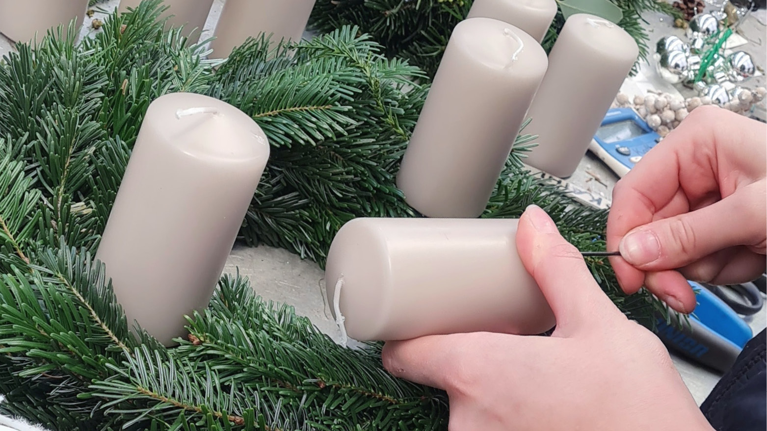 Ein Adventkranz mit wei&szlig;en Kerzen wird gebunden