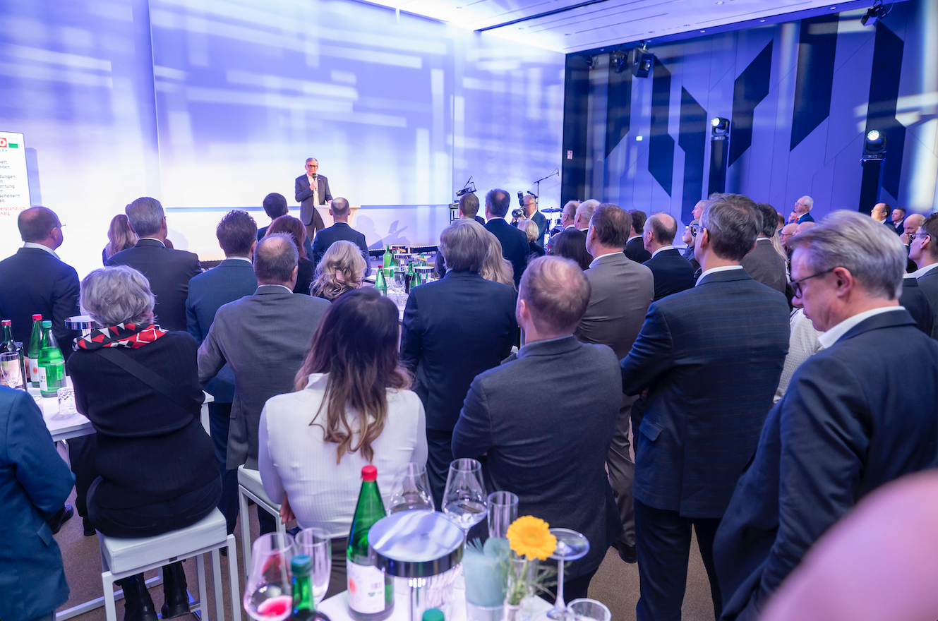 Viele Zuh&ouml;rer und im Hintergrund Josef Herk bei seiner Rede auf der B&uuml;hne