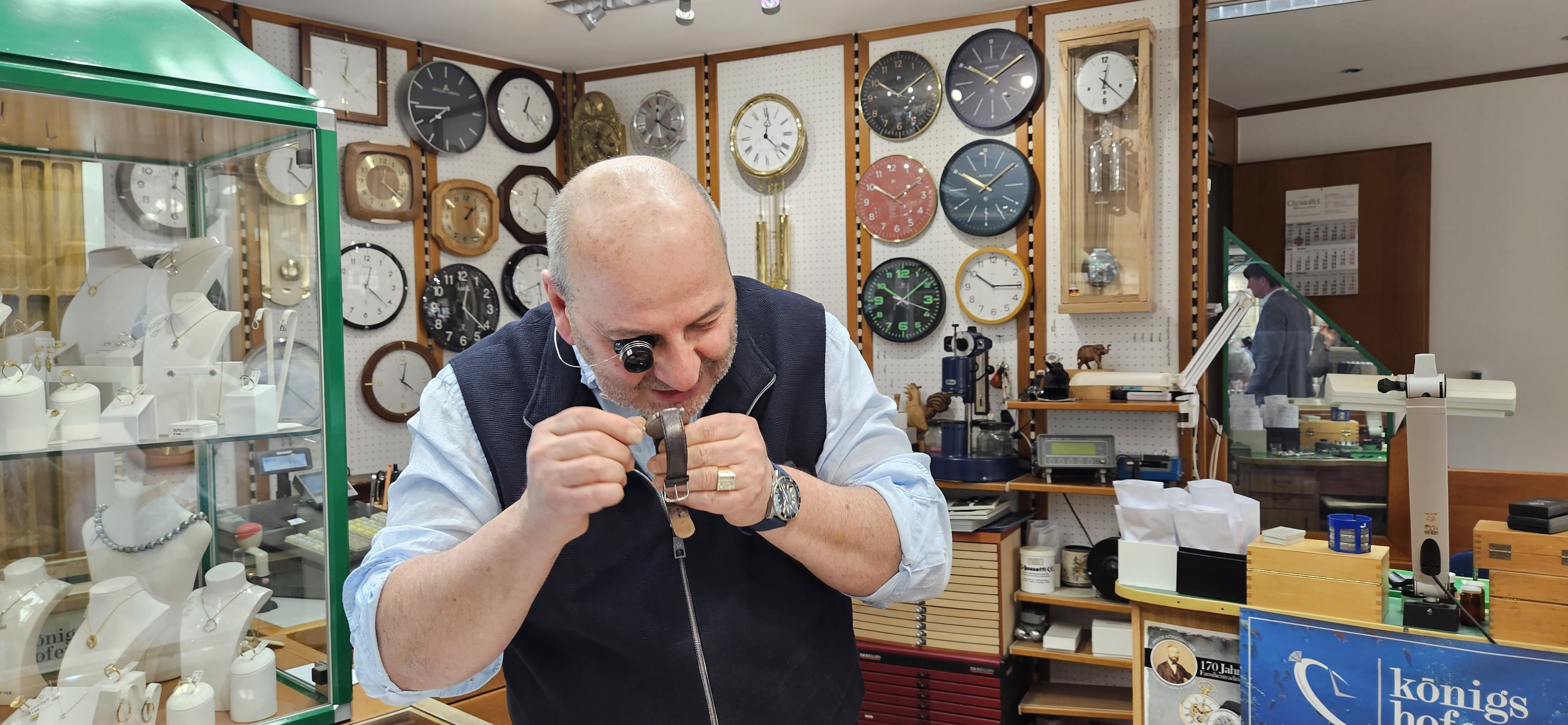 Josef Königshofer steht vor zahlreichen Uhren und untersucht eine gerade genau