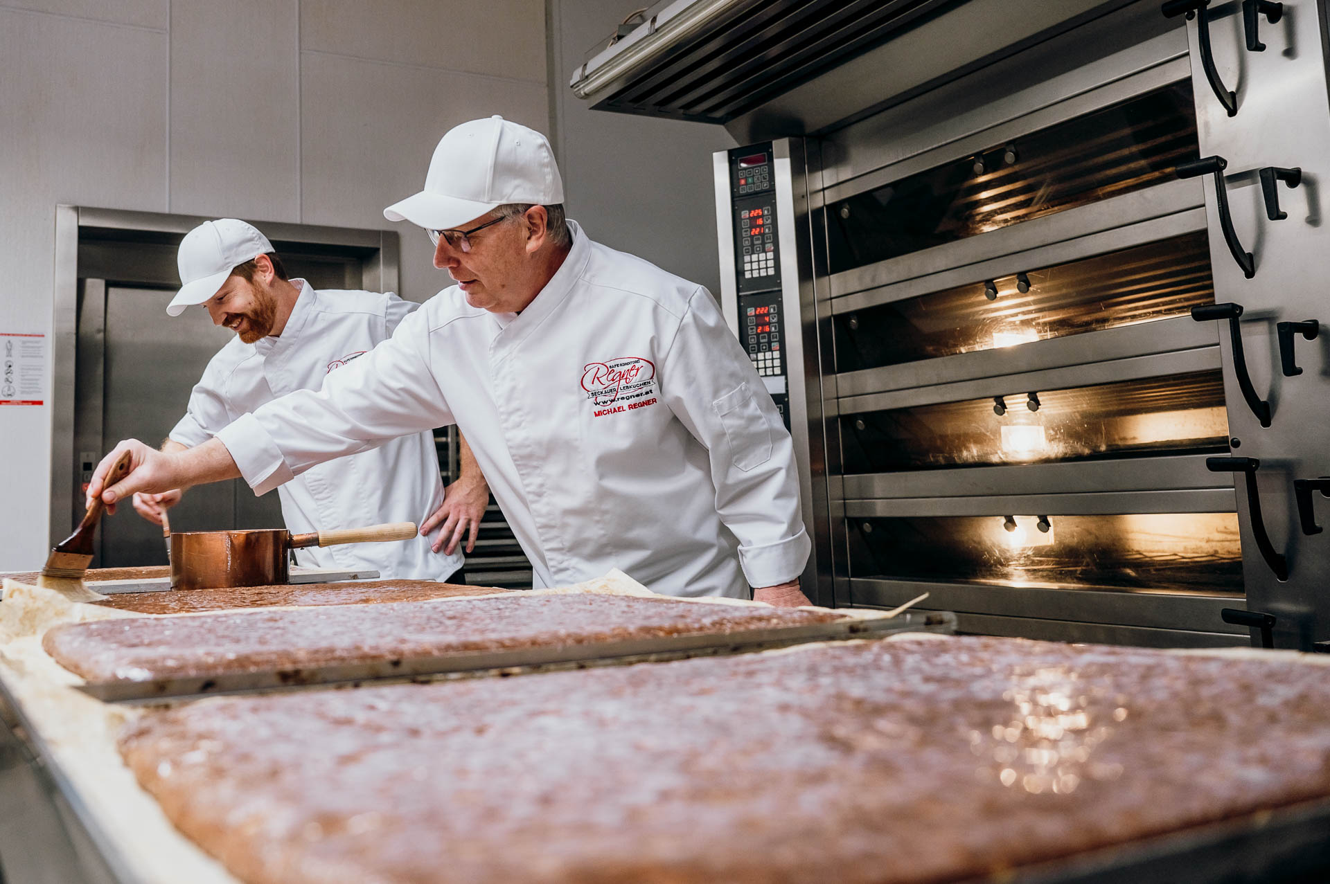 Zwei M&auml;nner bestreichen Lebkuchenteig