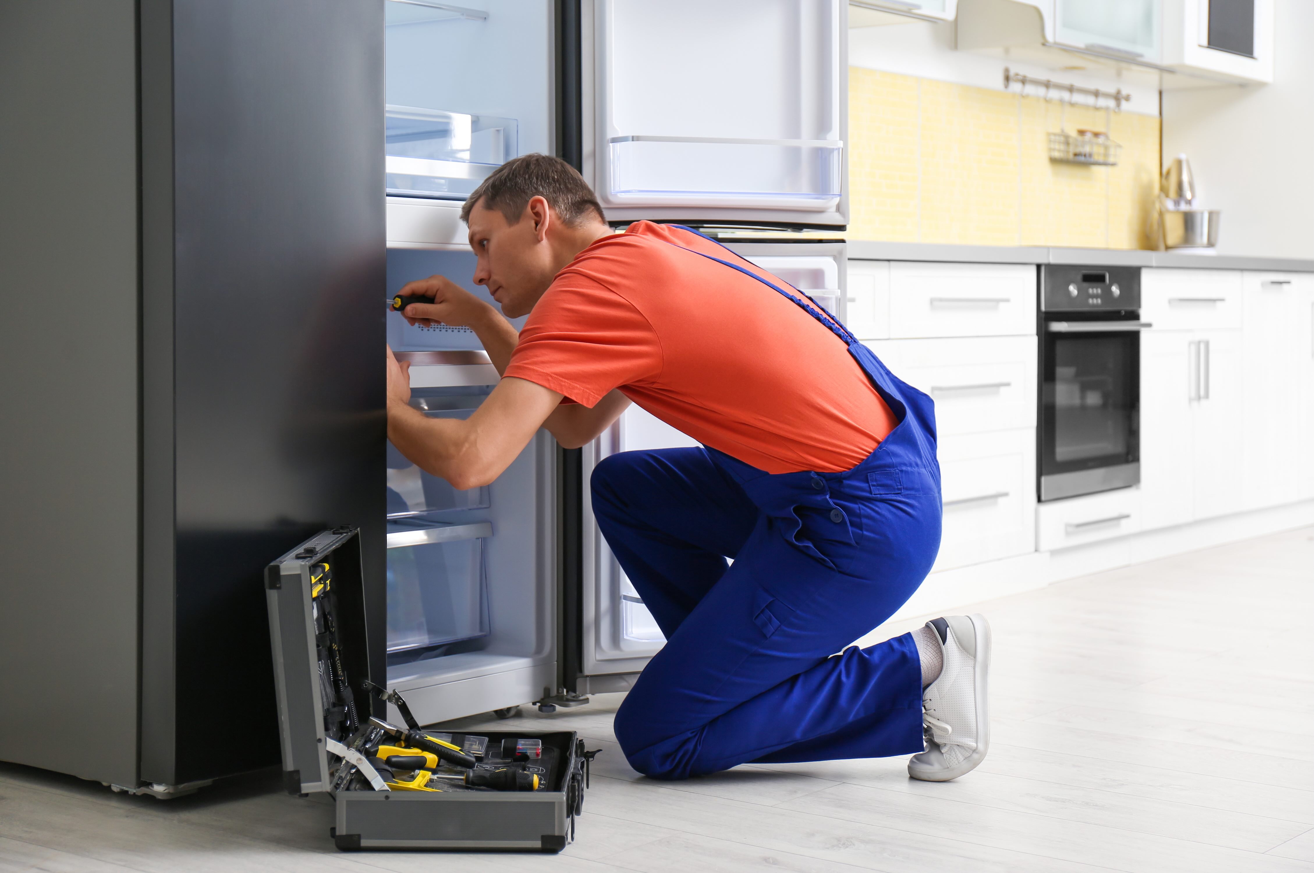 Servicetechniker repariert einen K&uuml;hlschrank mit einem Schraubendreher in einer K&uuml;che.