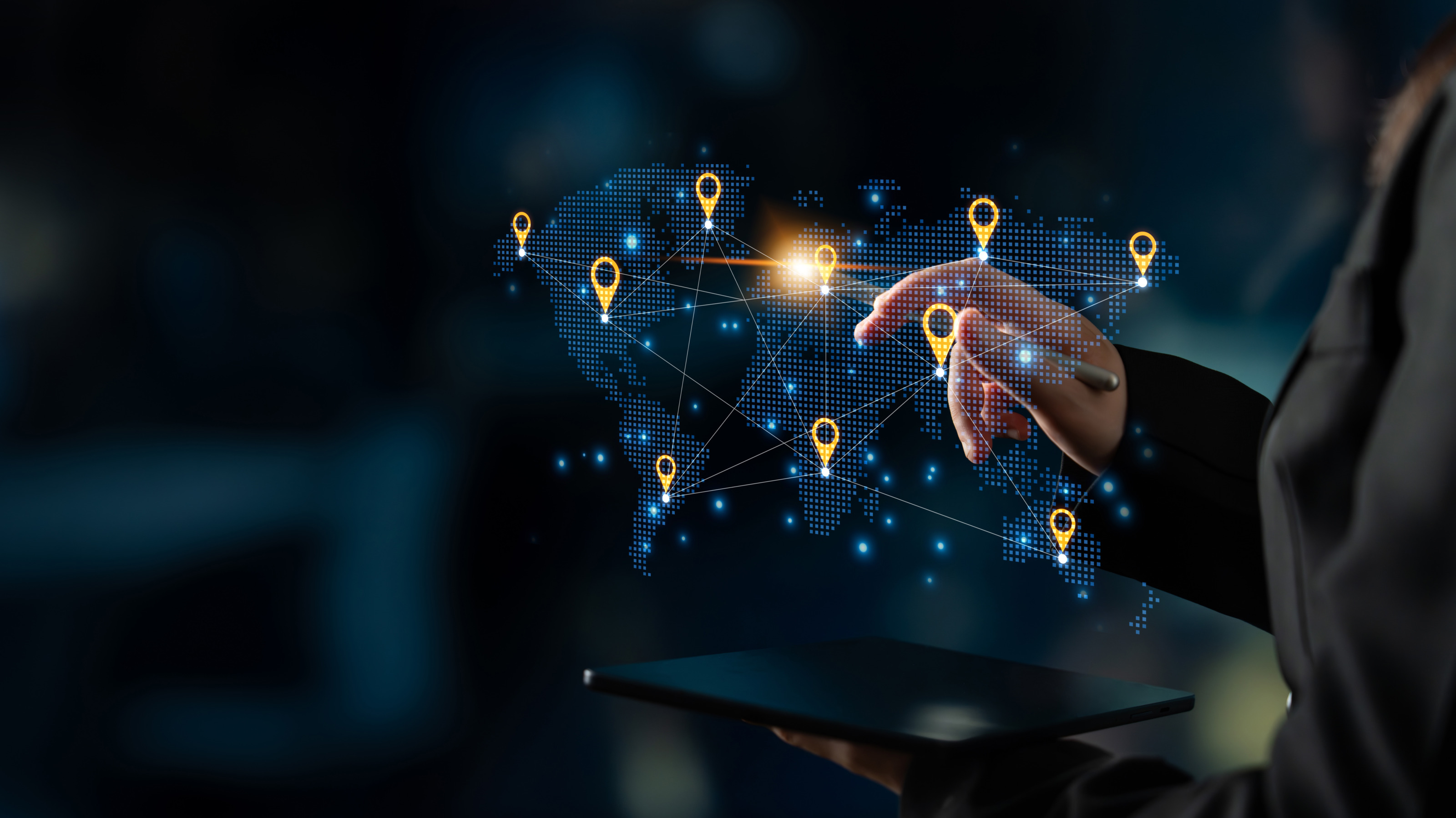 In der Mitte des Bildes ist eine Grafik der Kontinente der Welt. An manchen Stellen sind Icons f&uuml;r Lokalisierungen, die miteinander verbunden sind. Die rechte Hand einer Person zeigt mit einem Stift auf eine Stelle