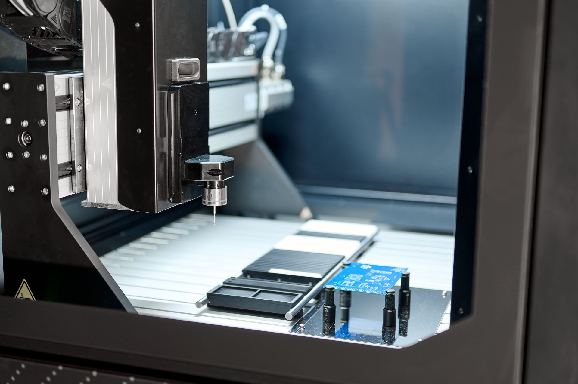 Rechts liegt eine blaue Platine in der Maschine, links sieht man eine Nadel