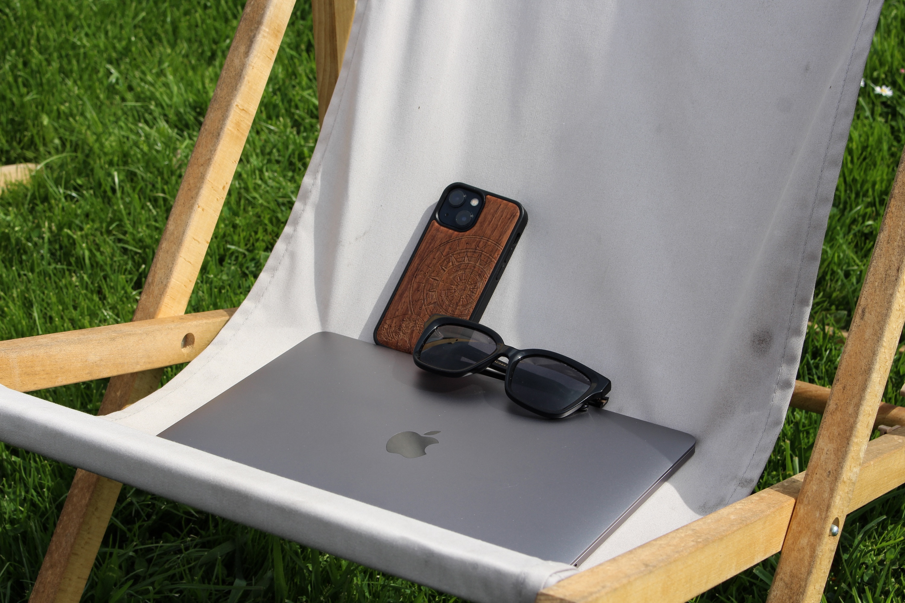 Liegestuhl. Darauf ist ein Handy, eine Sonnenbrille und ein Laptop platziert.