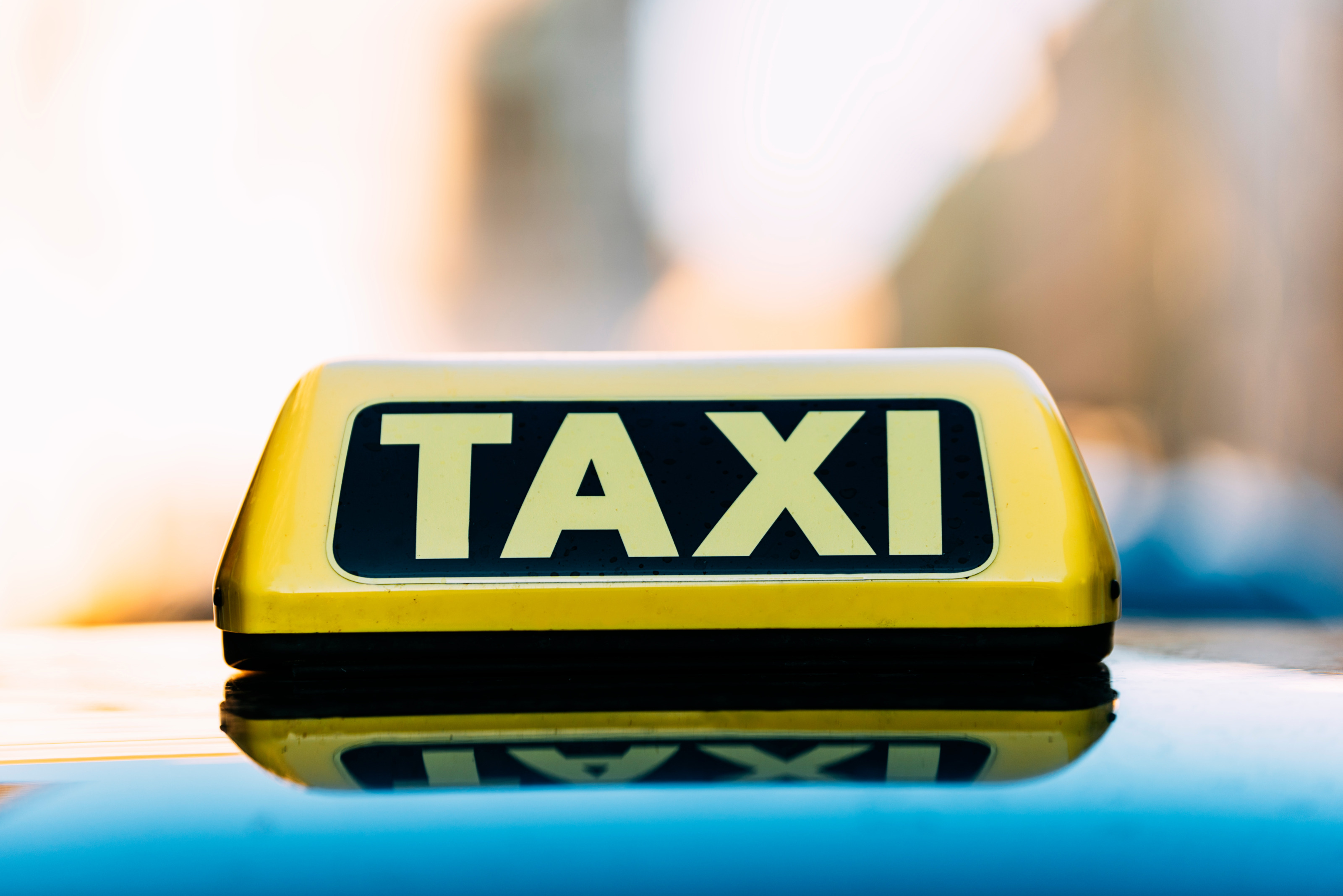 Leuchtend gelbes Zeichen auf Autodach: Gelber länglicher Leuchtkörper mit schwarzen Elementen und Schriftzug Taxi spiegelt sich in Autodach